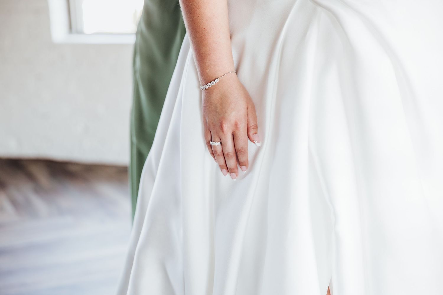 Close-up detail of a flowing white wedding dress fabric against a light background.