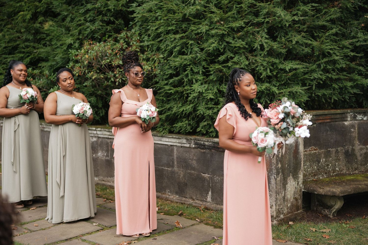 Bridesmaids in peach and beige dresses holding bouquets at an outdoor wedding.