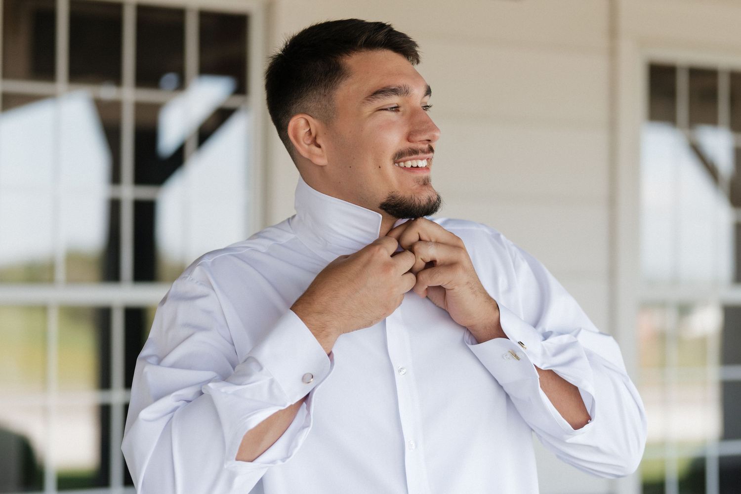 Groomsmen in black suits and red ties share joyful laughter while getting ready for a wedding celebration.