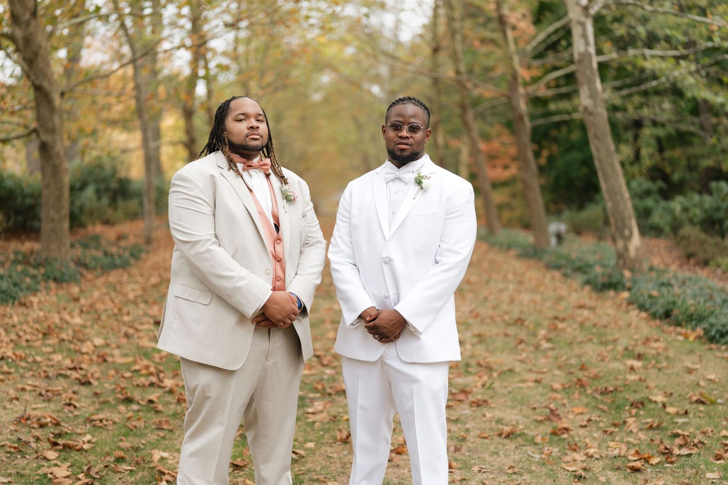 Wedding party members in white suits pose together on autumn grounds.