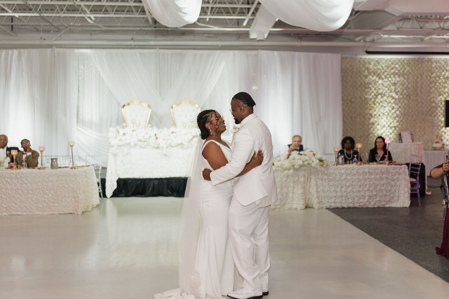 A couple shares their first dance in an elegant white-decorated reception hall.