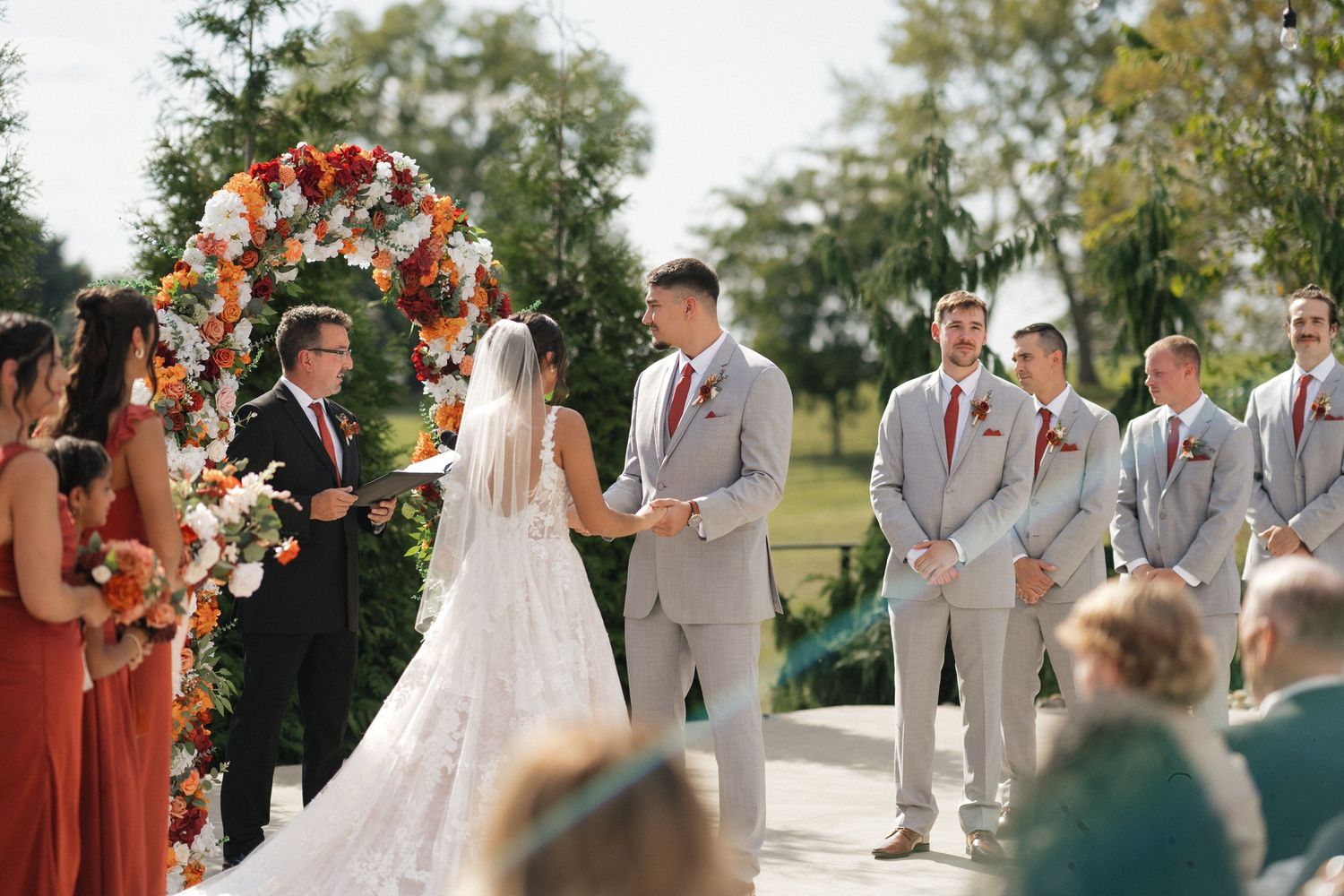 Outdoor wedding ceremony with bridal party in light gray and coral attire.