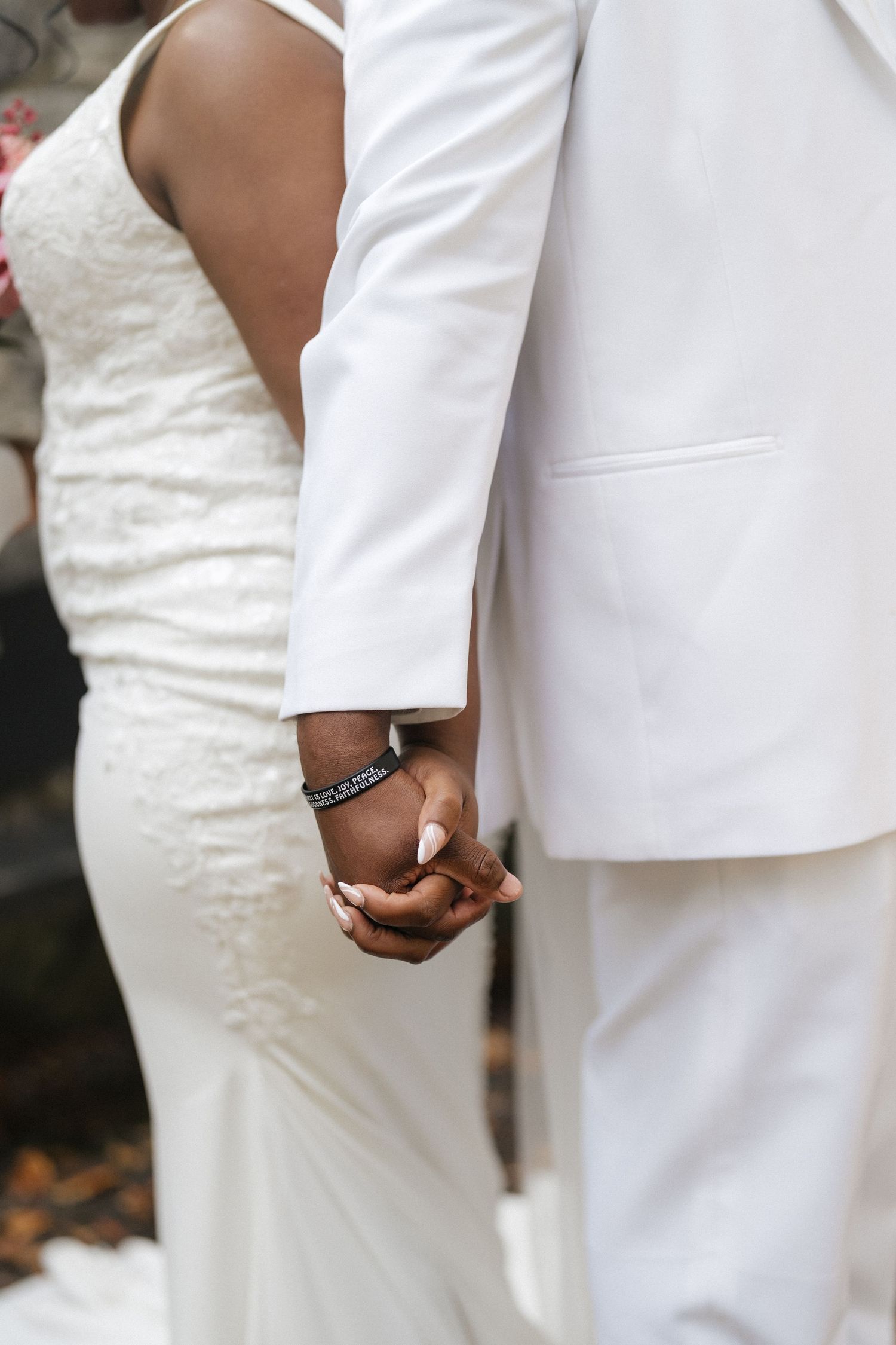 Close-up of a couple holding hands, with the bride in white lace and groom in a white suit.