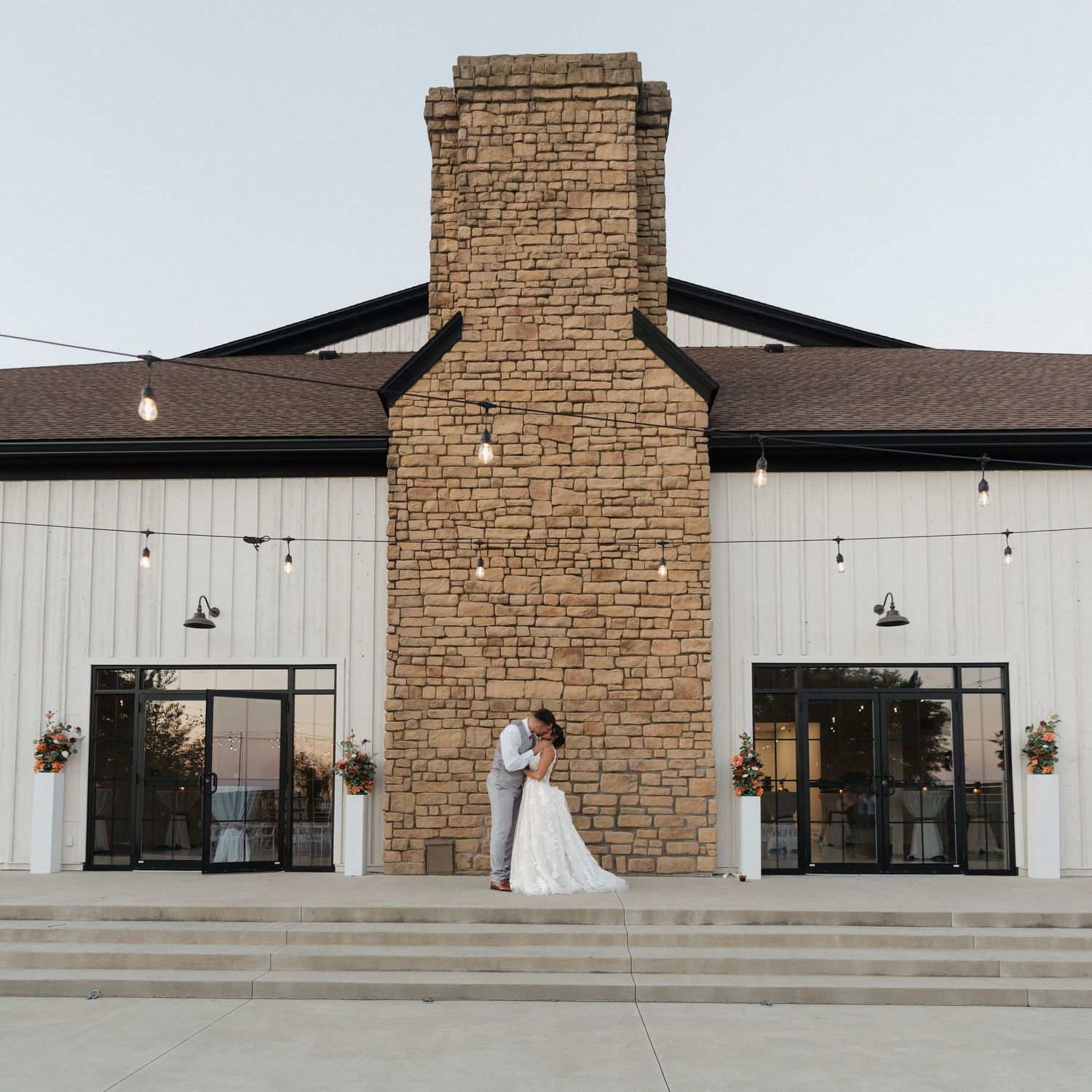 Modern stone venue exterior with string lights and large windows at dusk.