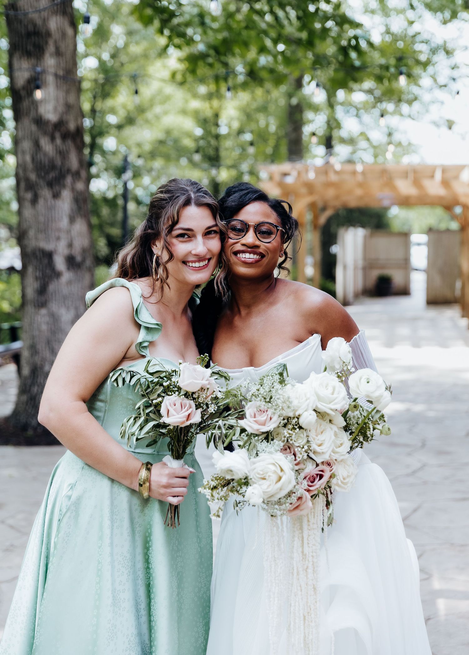 Bridesmaids in mint green dresses pose with white floral bouquets against natural outdoor backdrop.