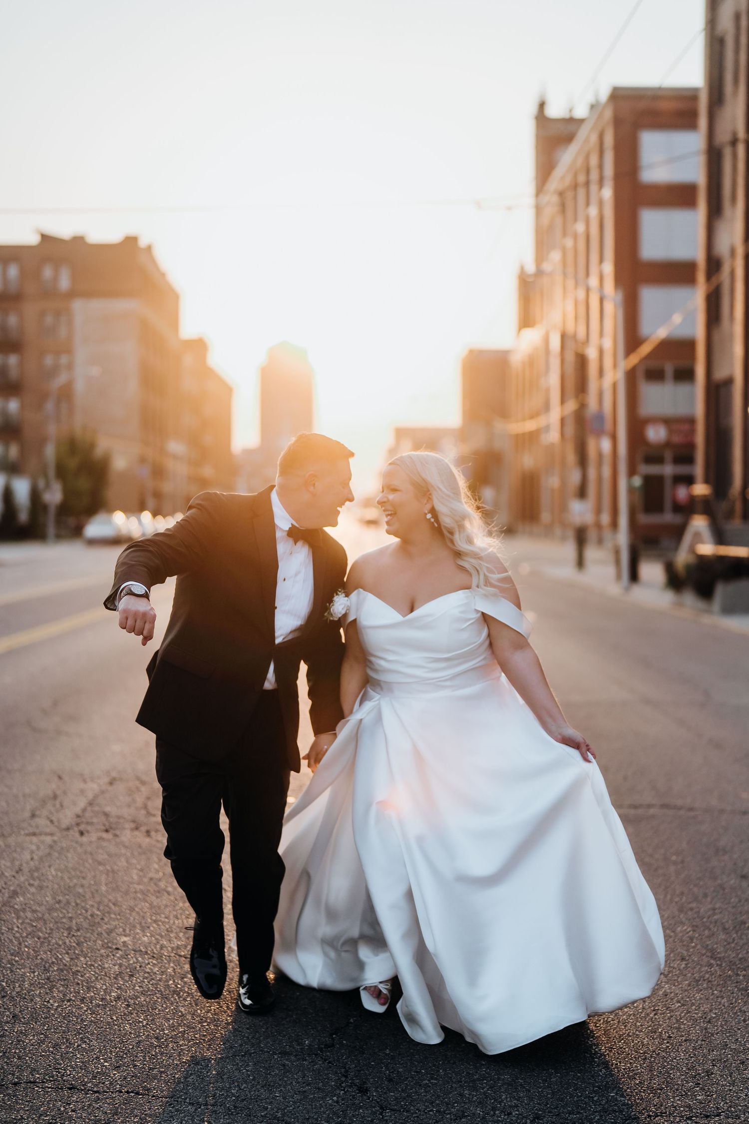 Wedding couple walking down a city street at sunset with flowing white dress.