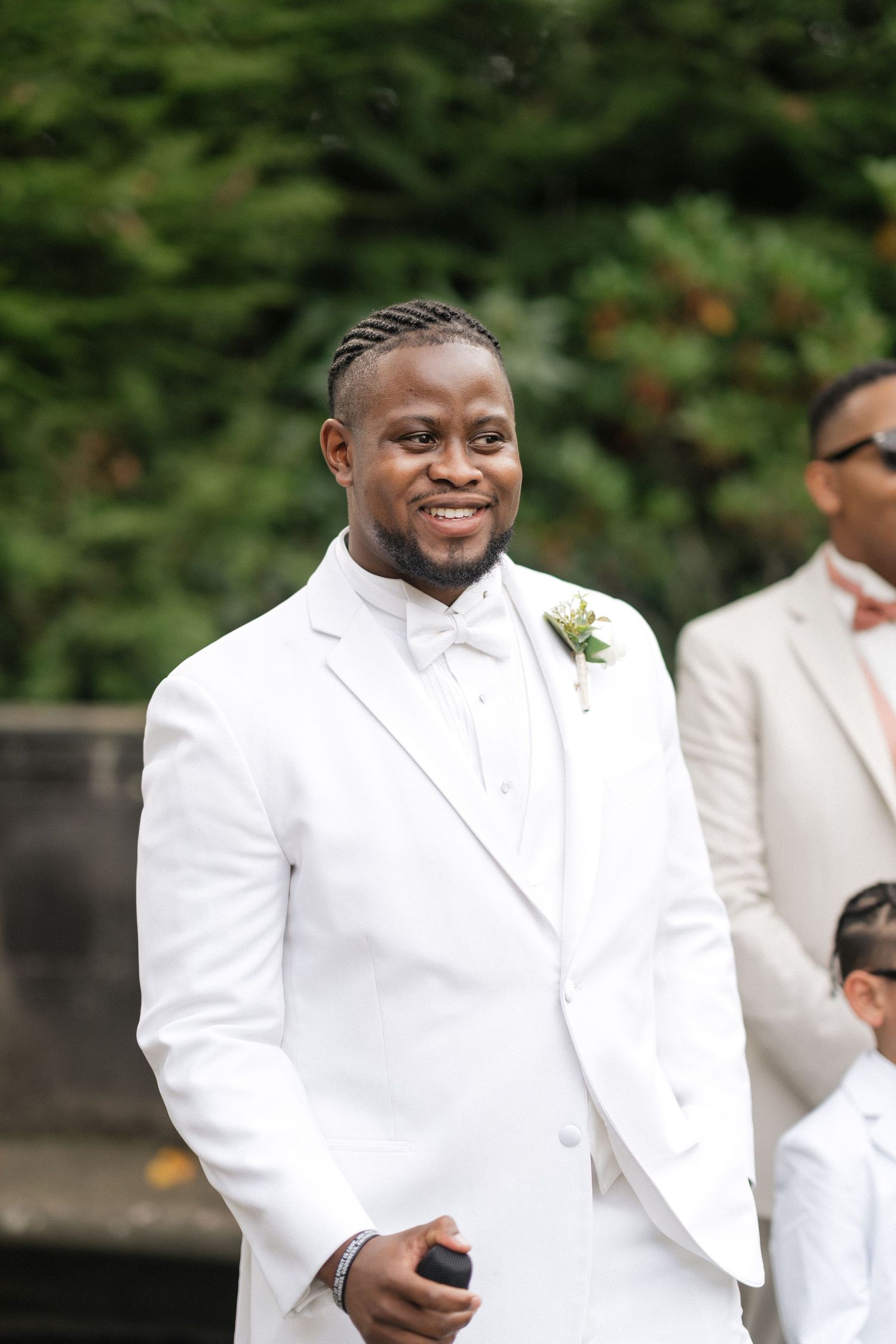Wedding party members in crisp white suits and boutonnieres smiling during an outdoor ceremony.
