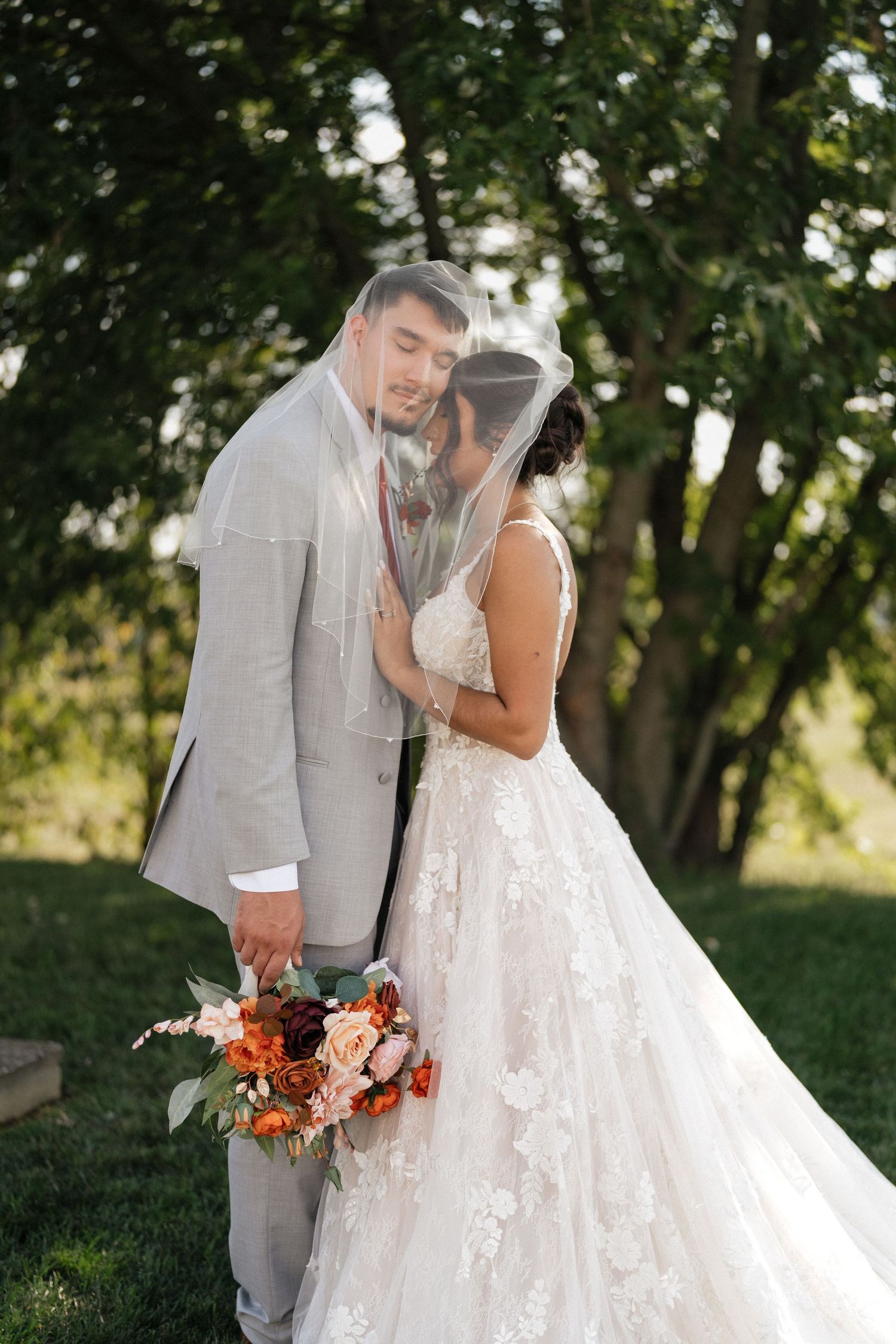 Romantic outdoor wedding portraits with bride in lace gown and groom in light gray suit.