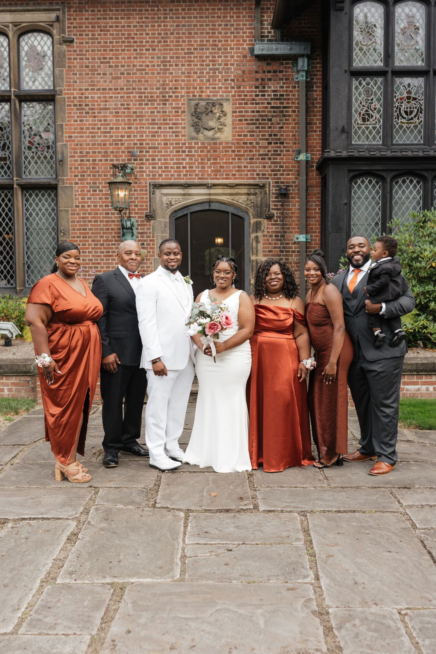 Wedding party poses in front of historic brick building with bridesmaids in rust-colored dresses.