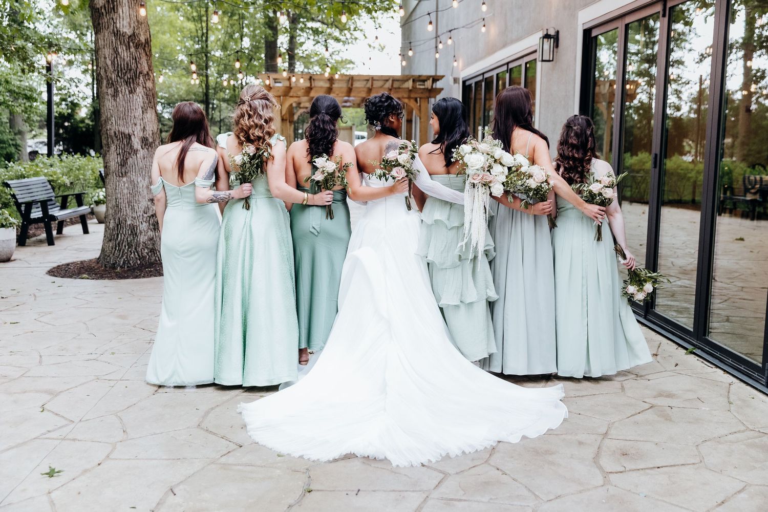 A bridal party in mint green dresses poses together outdoors with the bride in a white wedding gown.