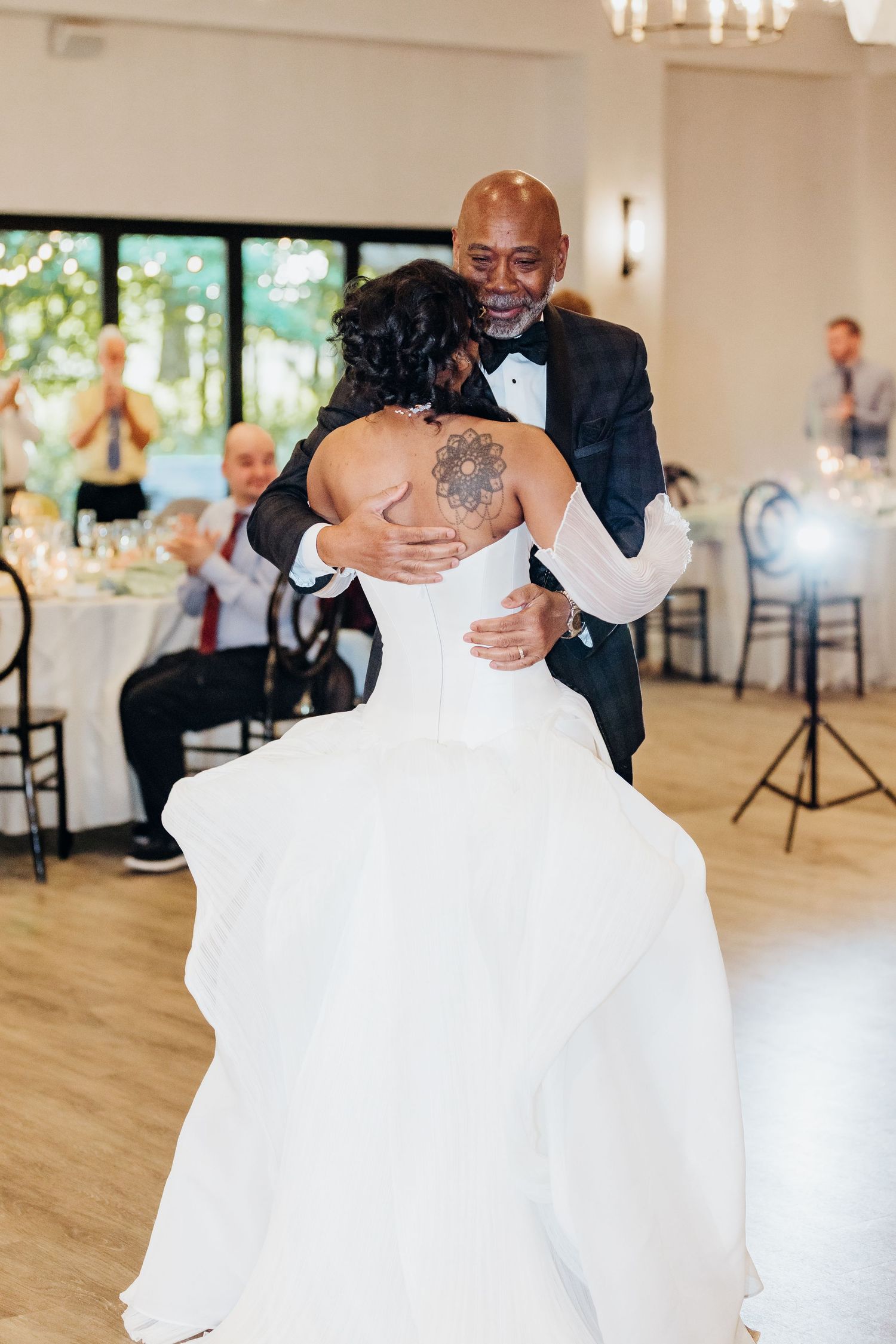 A couple dances together during their first dance at a wedding reception in an elegant white ballroom with hardwood floors.