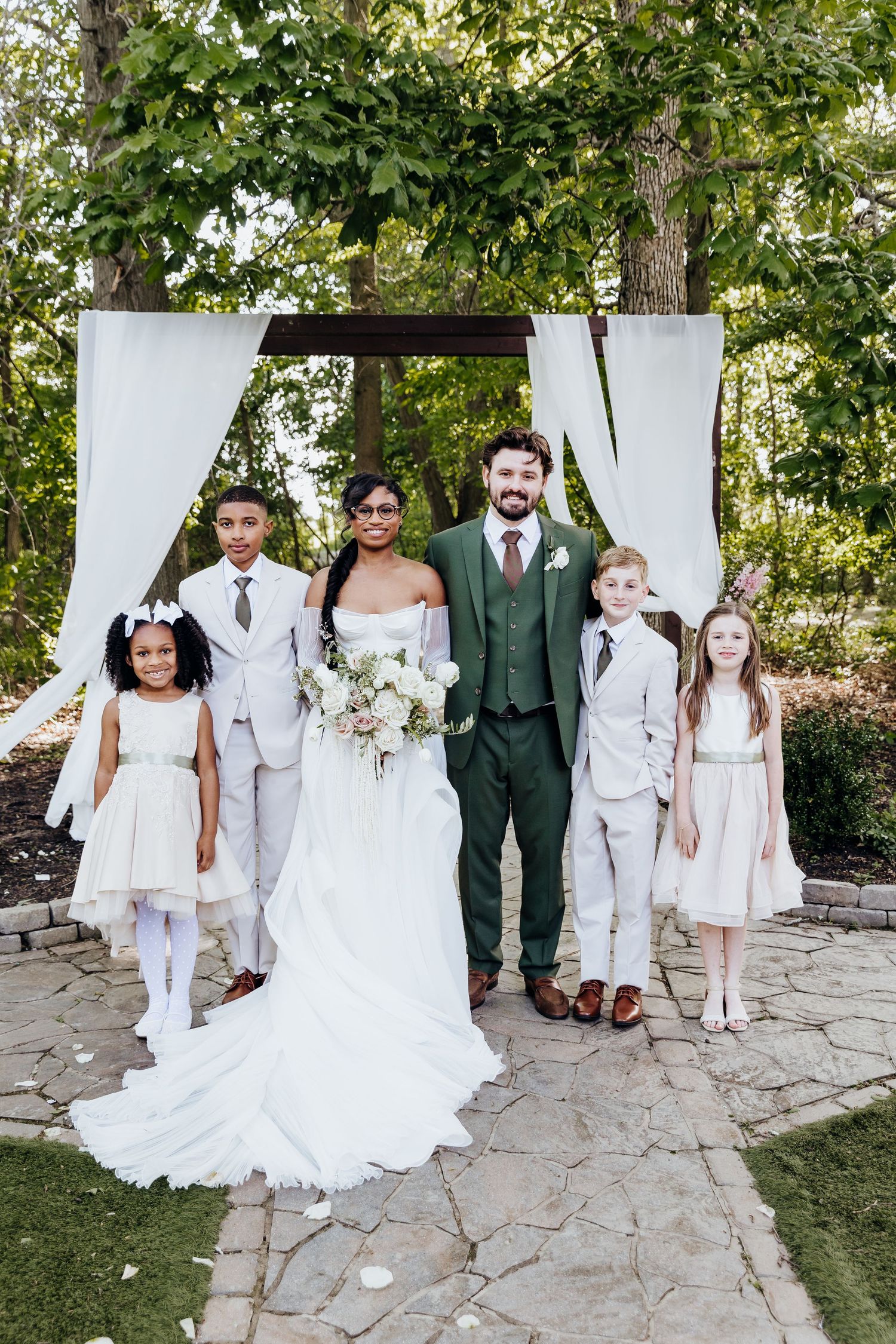 Wedding party poses on stone pathway with children in white attire and adults in green and white.