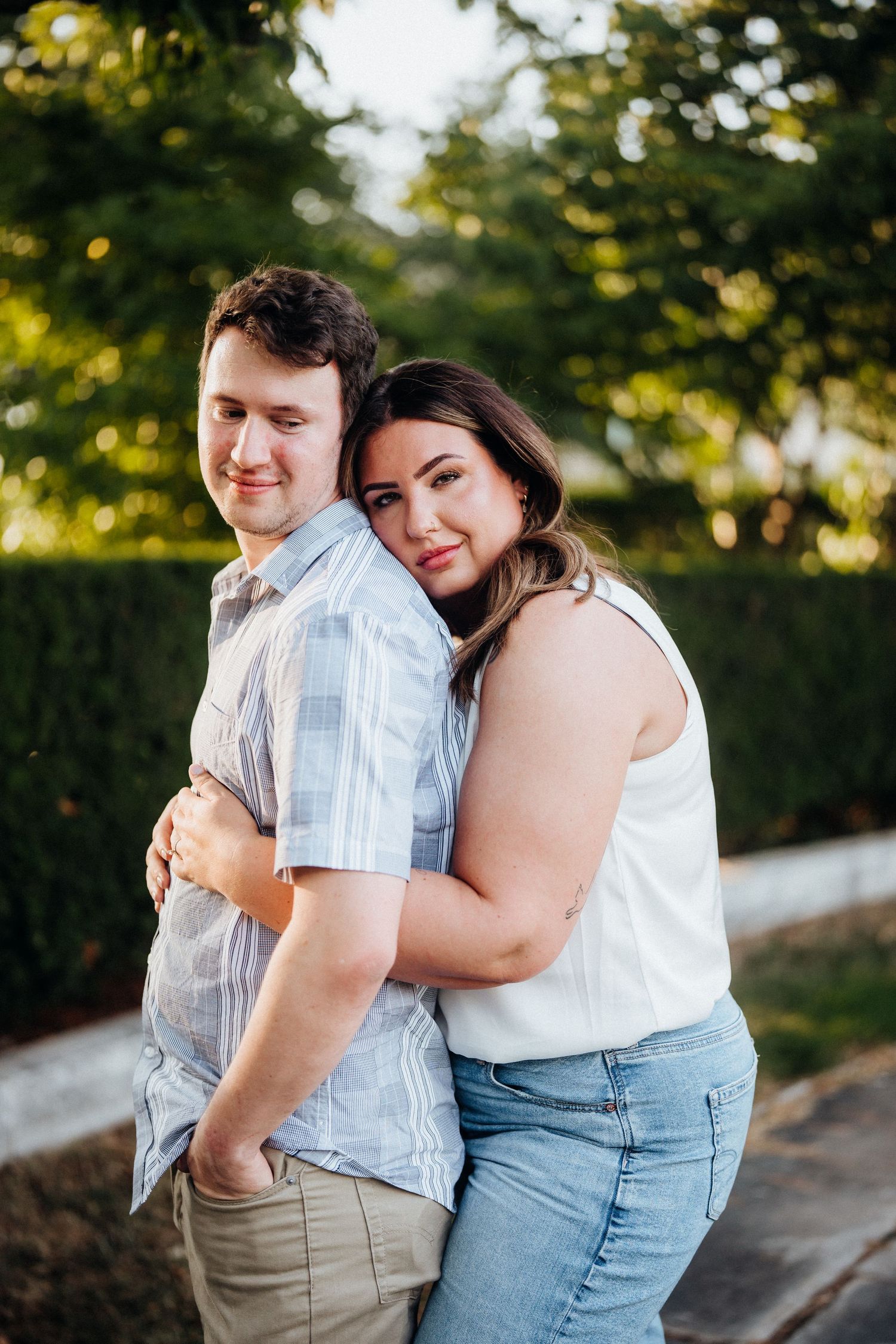 A romantic outdoor portrait of a couple embracing in a garden with warm sunlight filtering through trees.