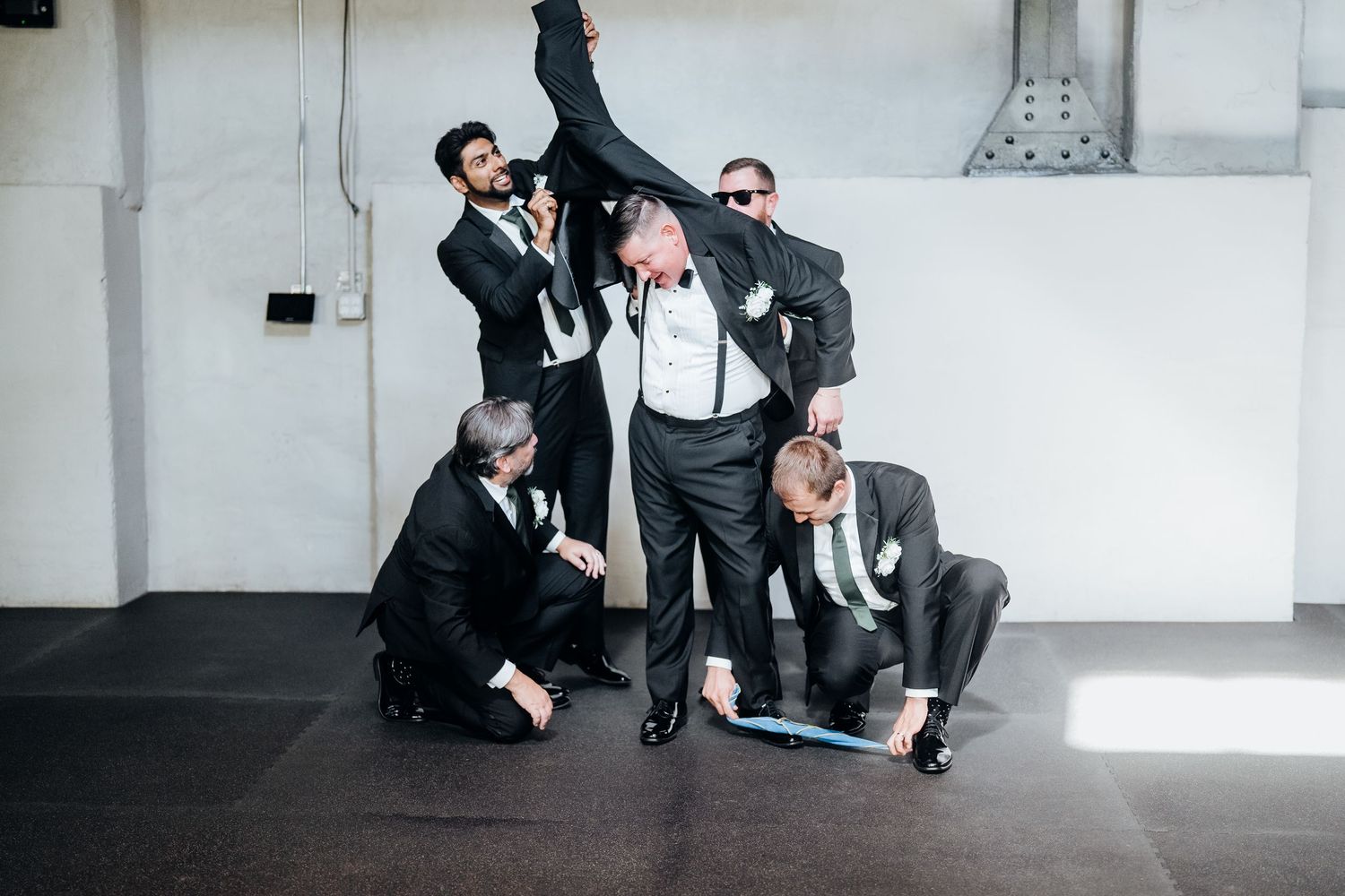 Groomsmen in black suits playfully posing and jumping during wedding photo session.