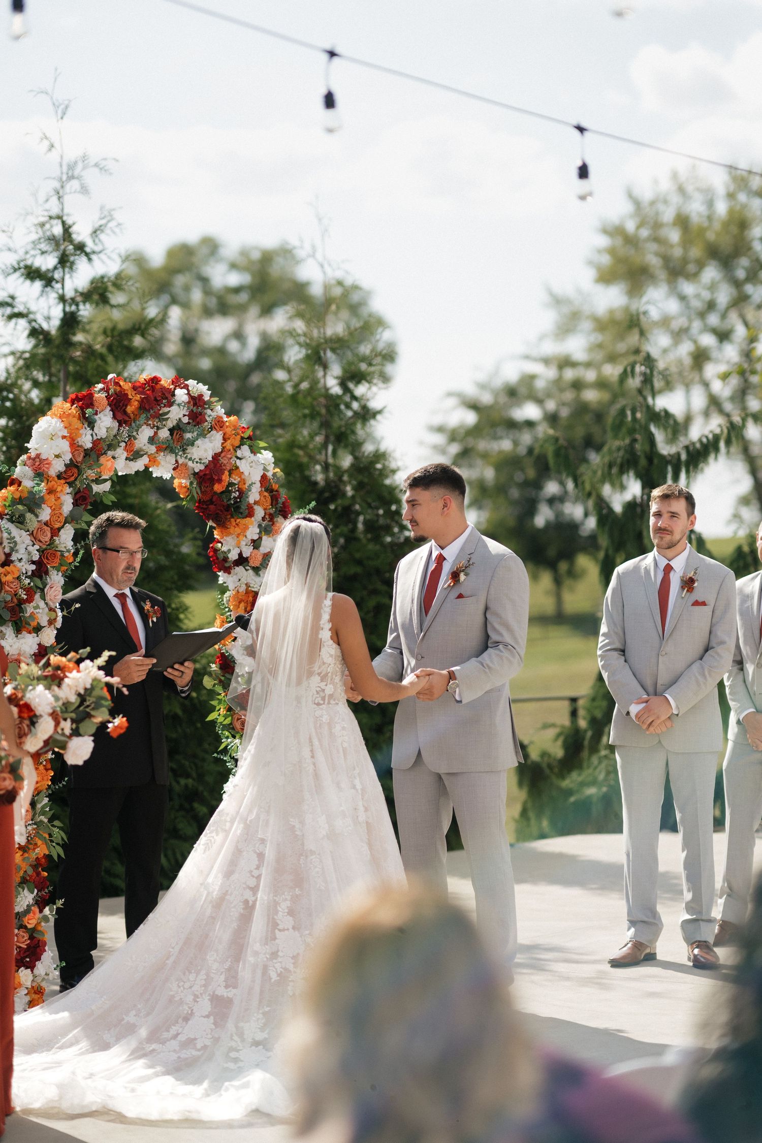 Outdoor wedding ceremony under floral arch with orange and white flowers.