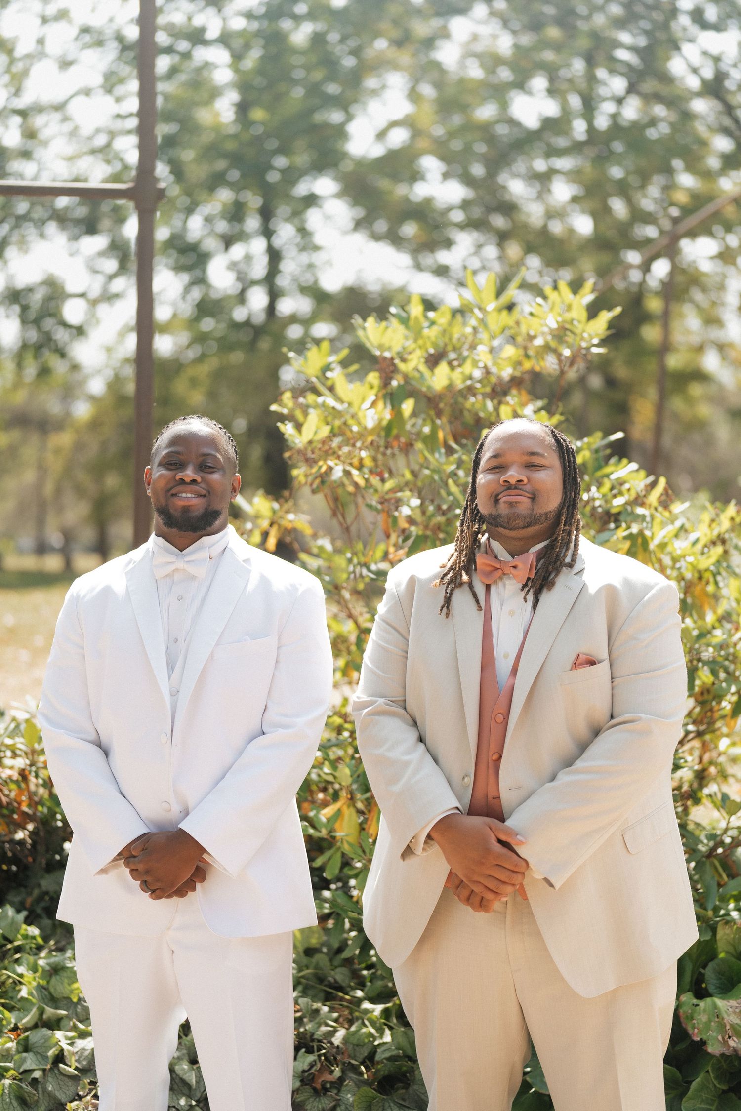 Groomsmen in crisp white suits pose together in a sunny garden setting.