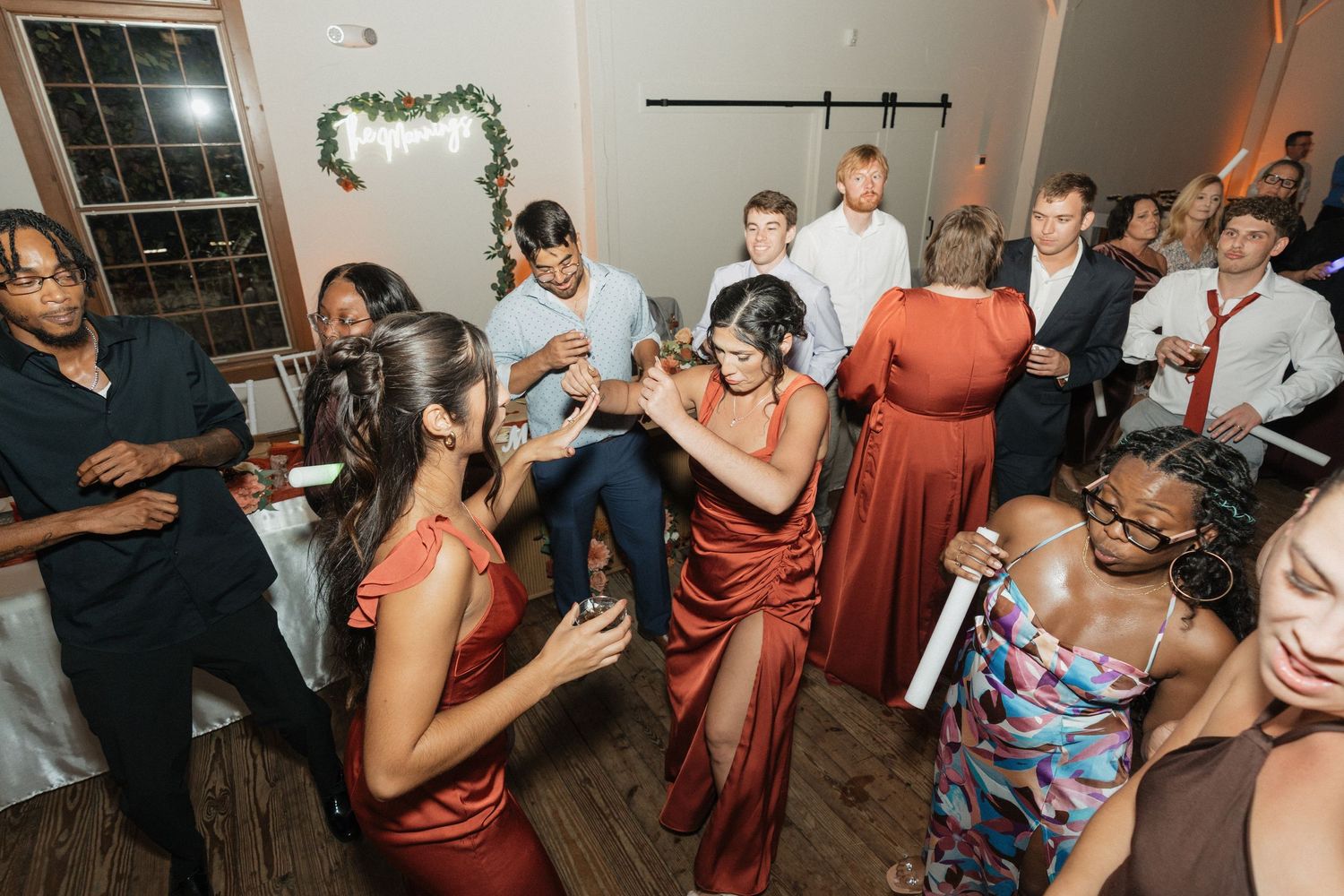 Wedding reception dance party with guests in burgundy dresses celebrating on dance floor.