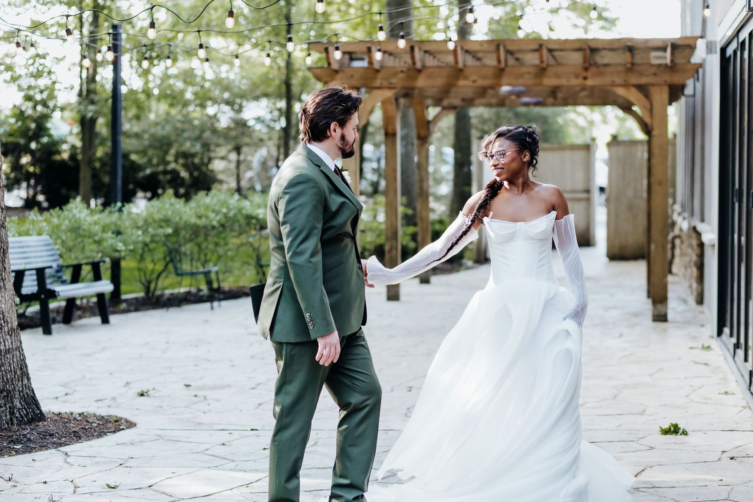 Couple shares their first look moment on a stone patio with wooden pergola in background.