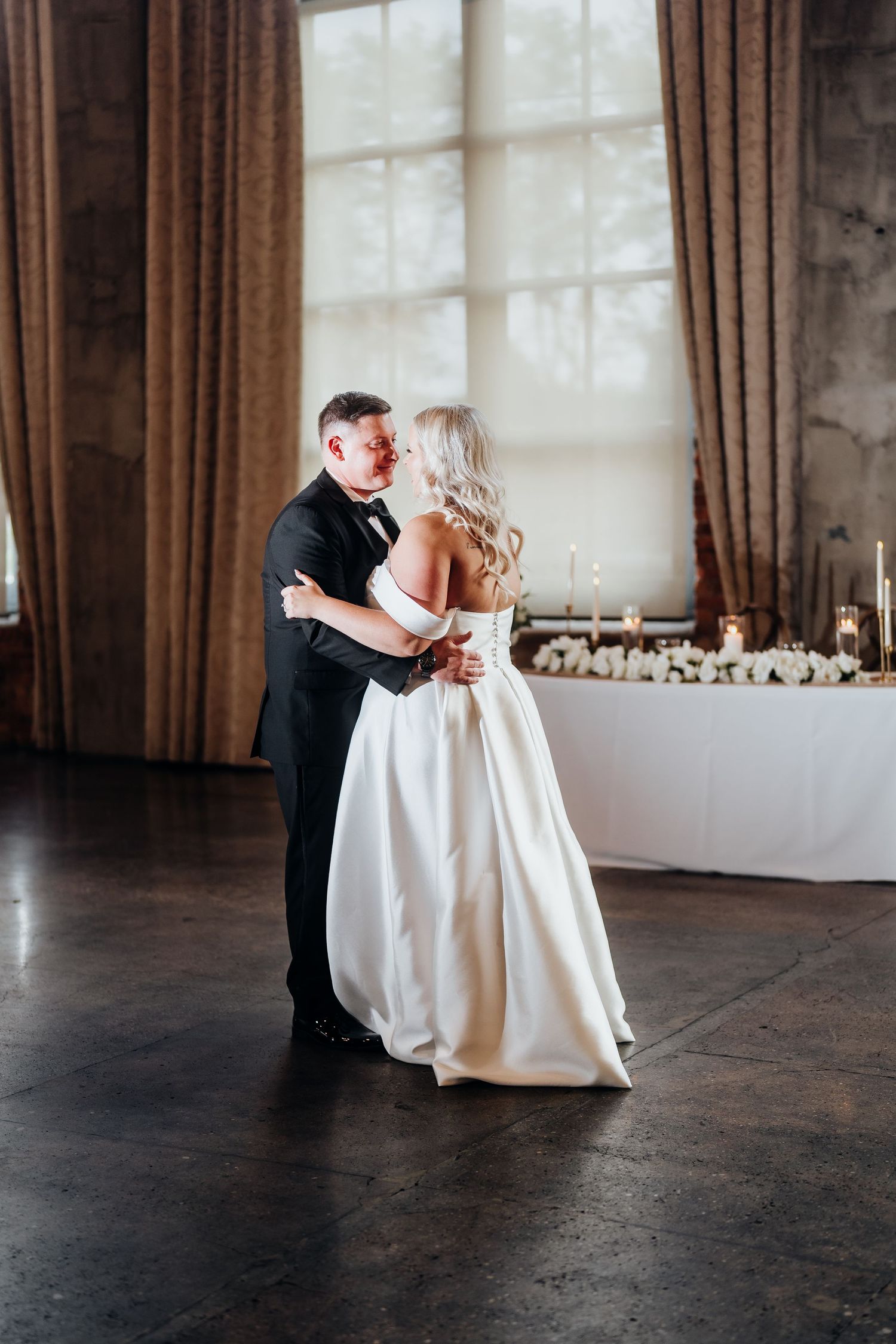 A romantic first dance moment in an elegant reception venue with large windows.