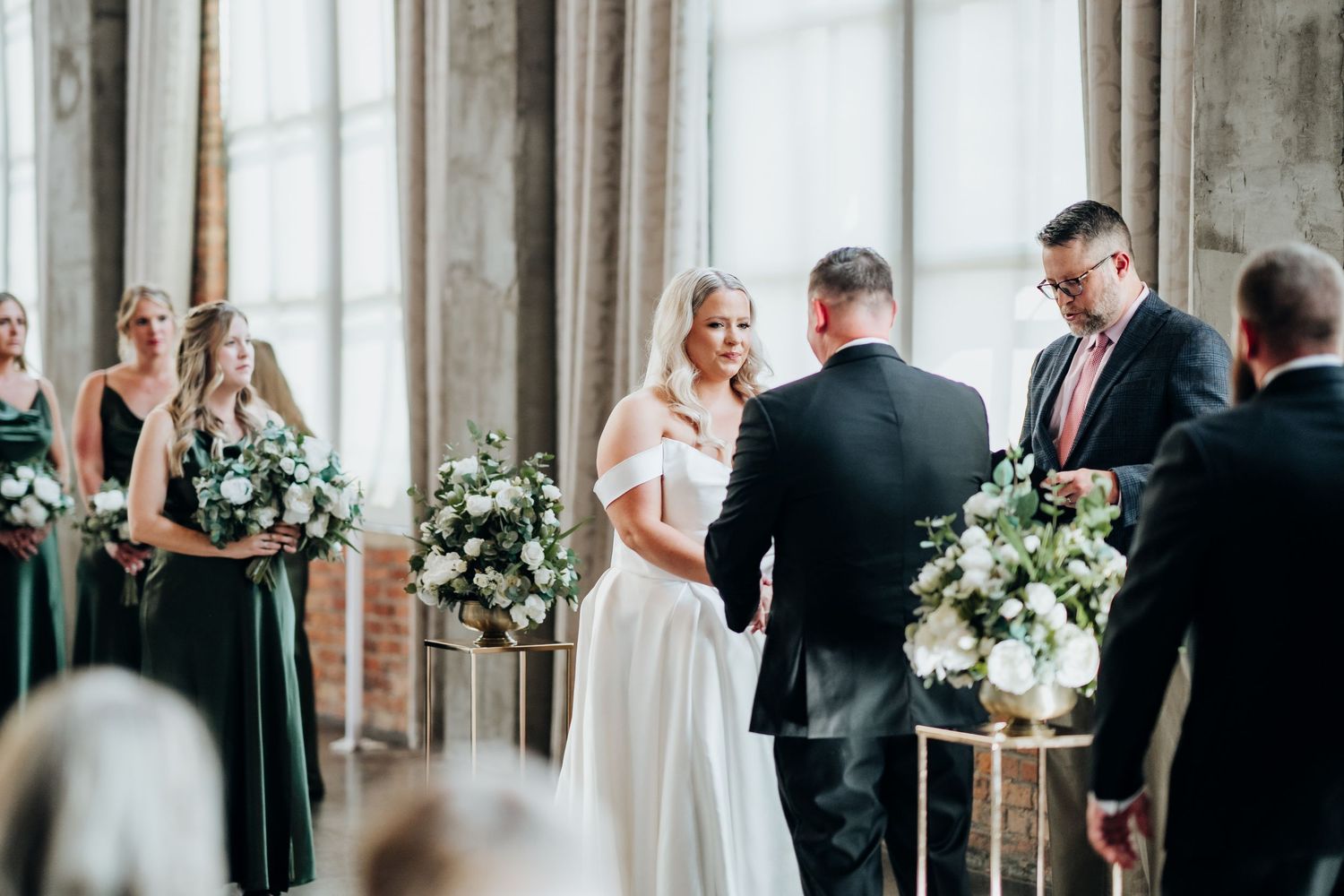 Wedding ceremony setup in bright industrial space with white curtains and floral arrangements.