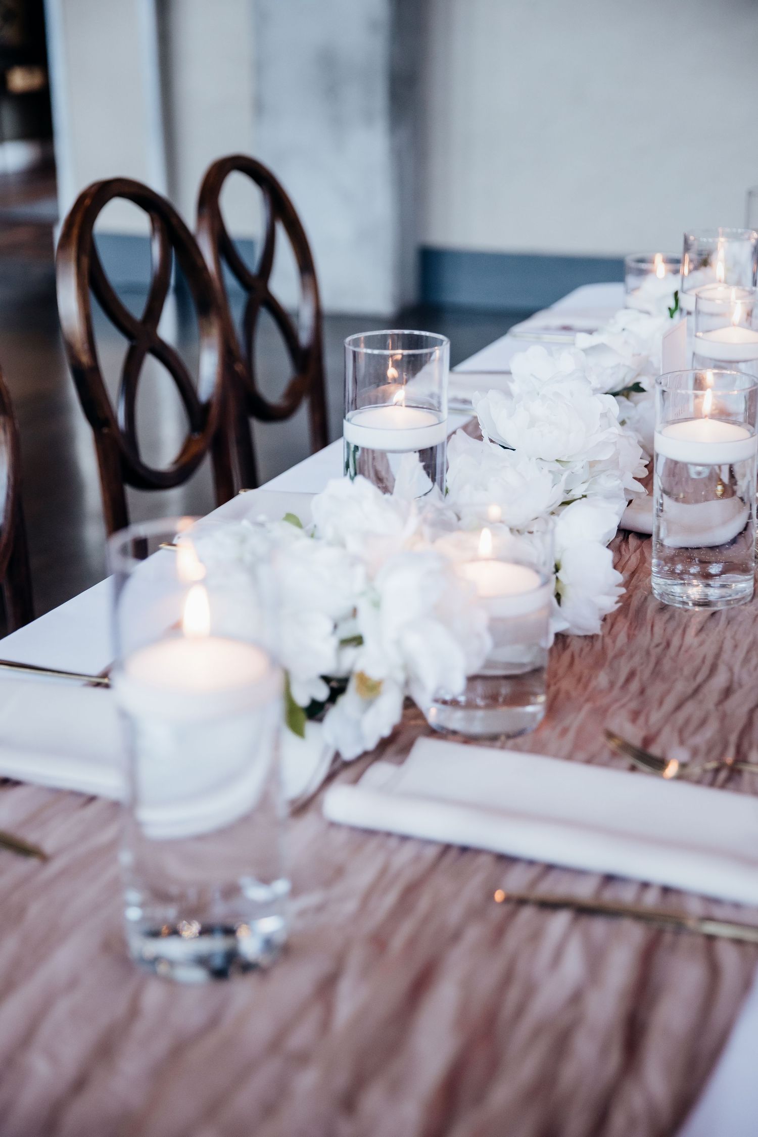 Elegant wedding table decor with white floral centerpieces and glowing candles on a brown tablecloth.