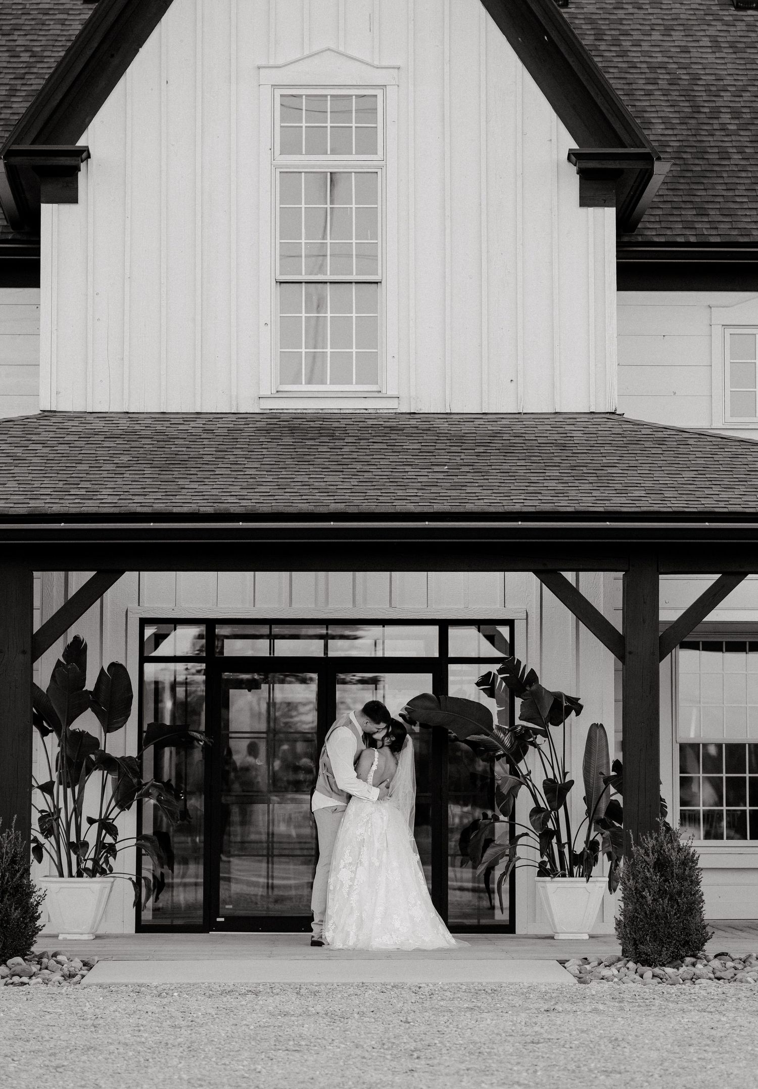 A black and white wedding photo in front of a modern white barn-style venue entrance.