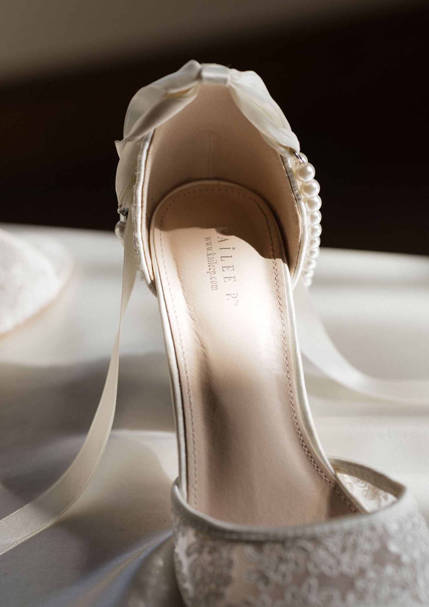 Elegant white bridal shoes with delicate details and straps displayed against a light background.
