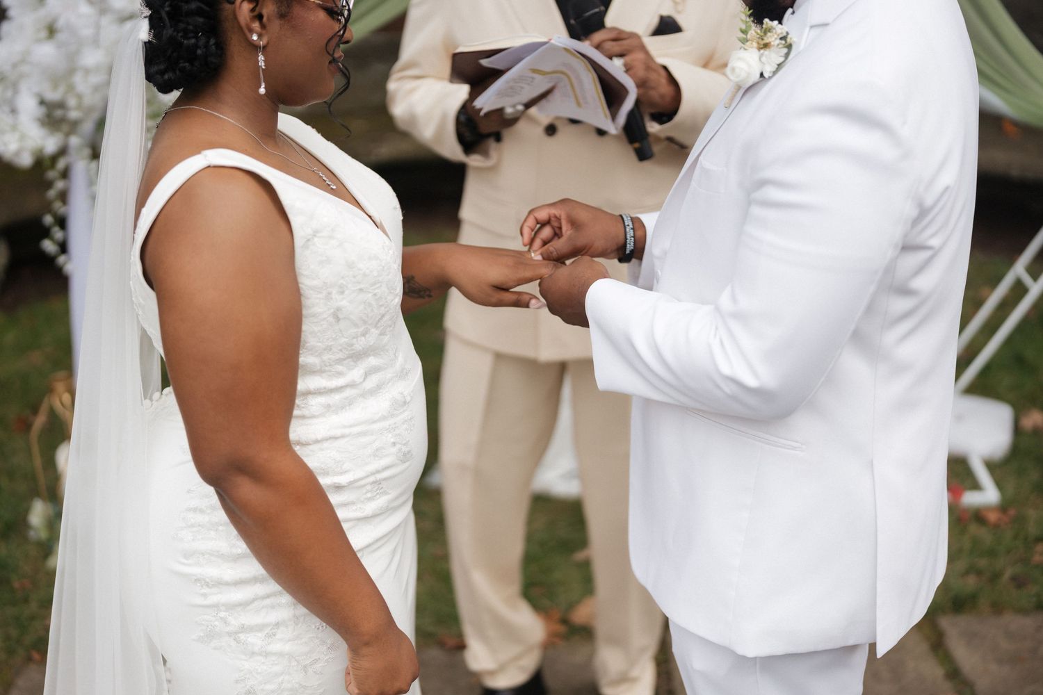 Wedding party in white and beige attire poses together outside a brick building.