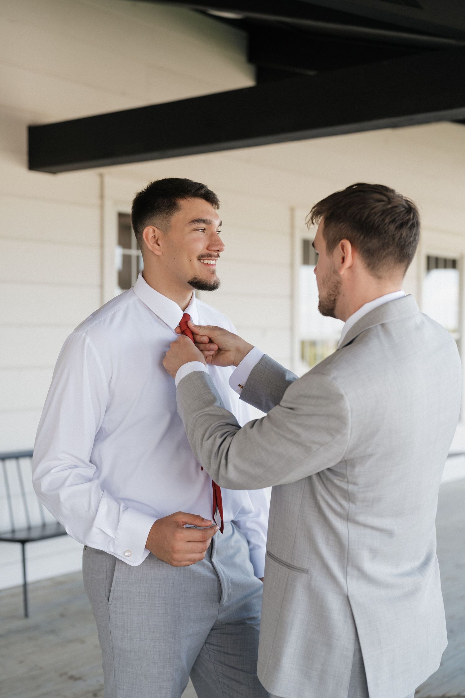 Two men in formal attire help adjust each other's ties and clothing before a special event.