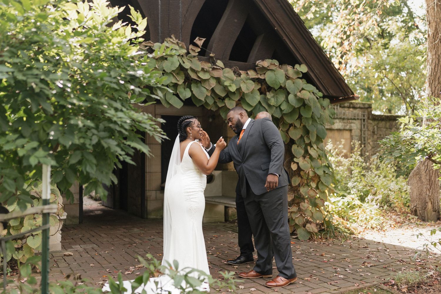 A couple shares an intimate moment under a vine-covered wooden gazebo during their wedding ceremony.