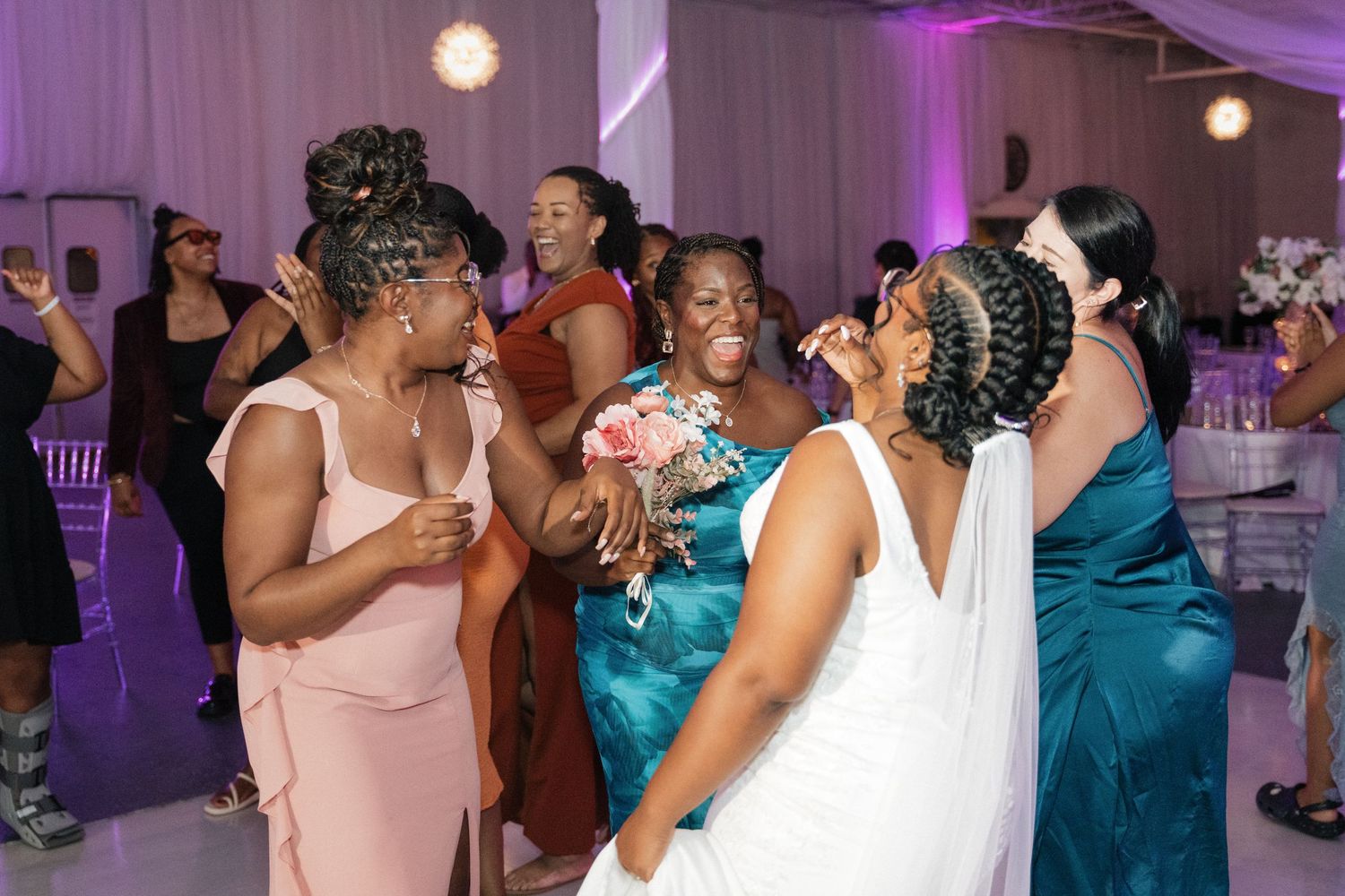 Wedding reception dance floor with guests dancing under purple ambient lighting.