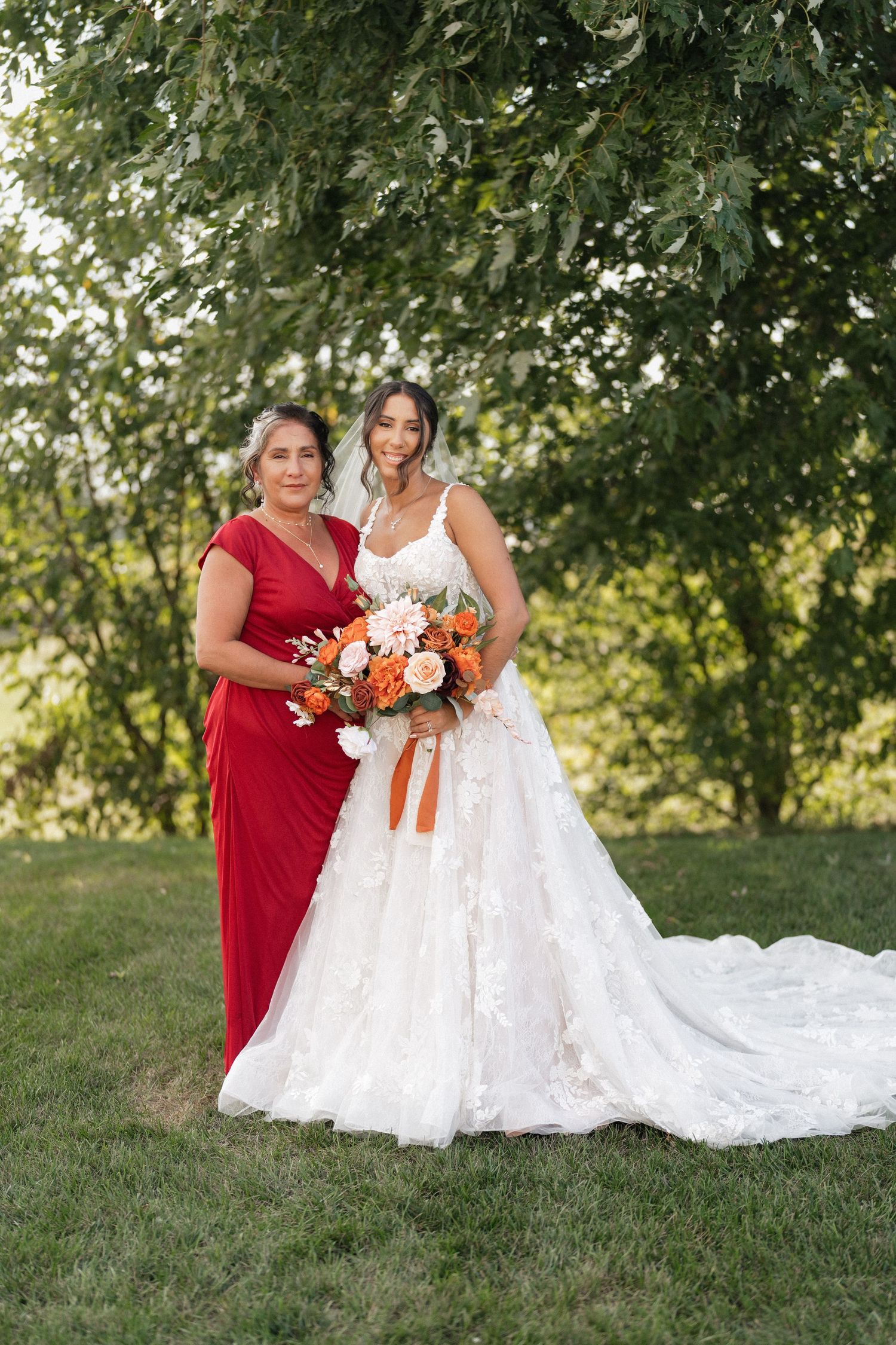 Wedding party members in red and white dresses posing on grassy hill with floral bouquets.