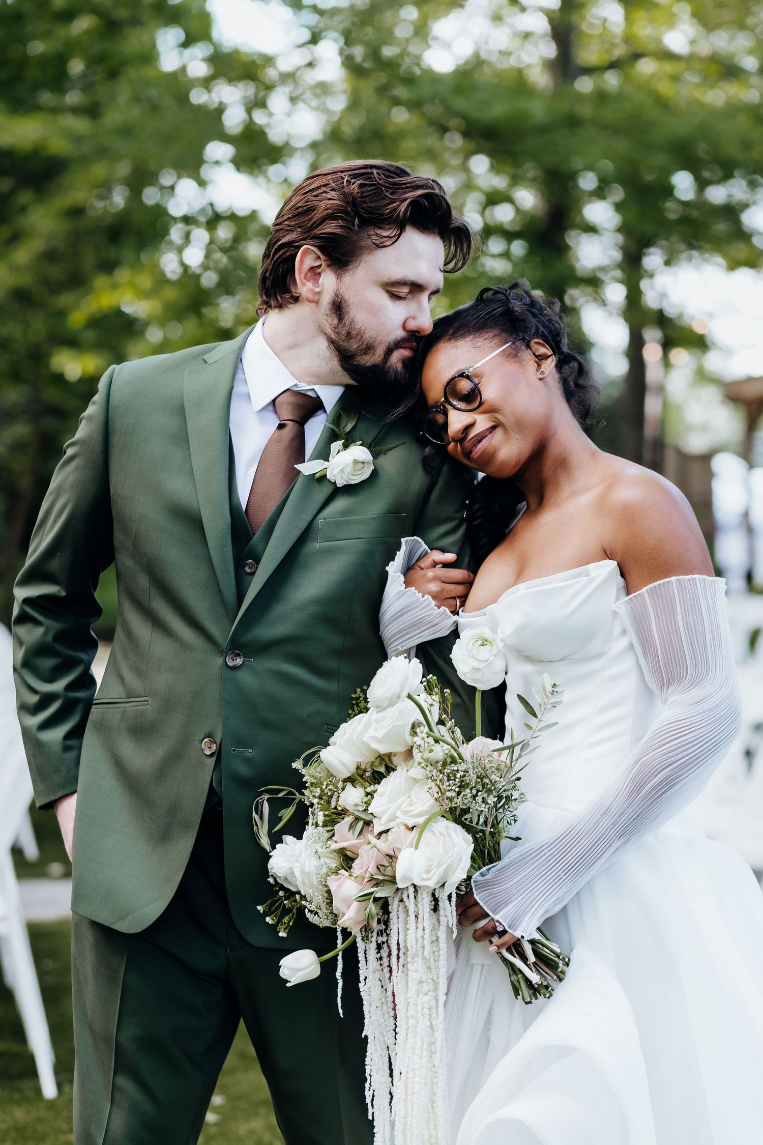 Romantic couple shares tender moments in garden setting with bride in white and groom in green suit.