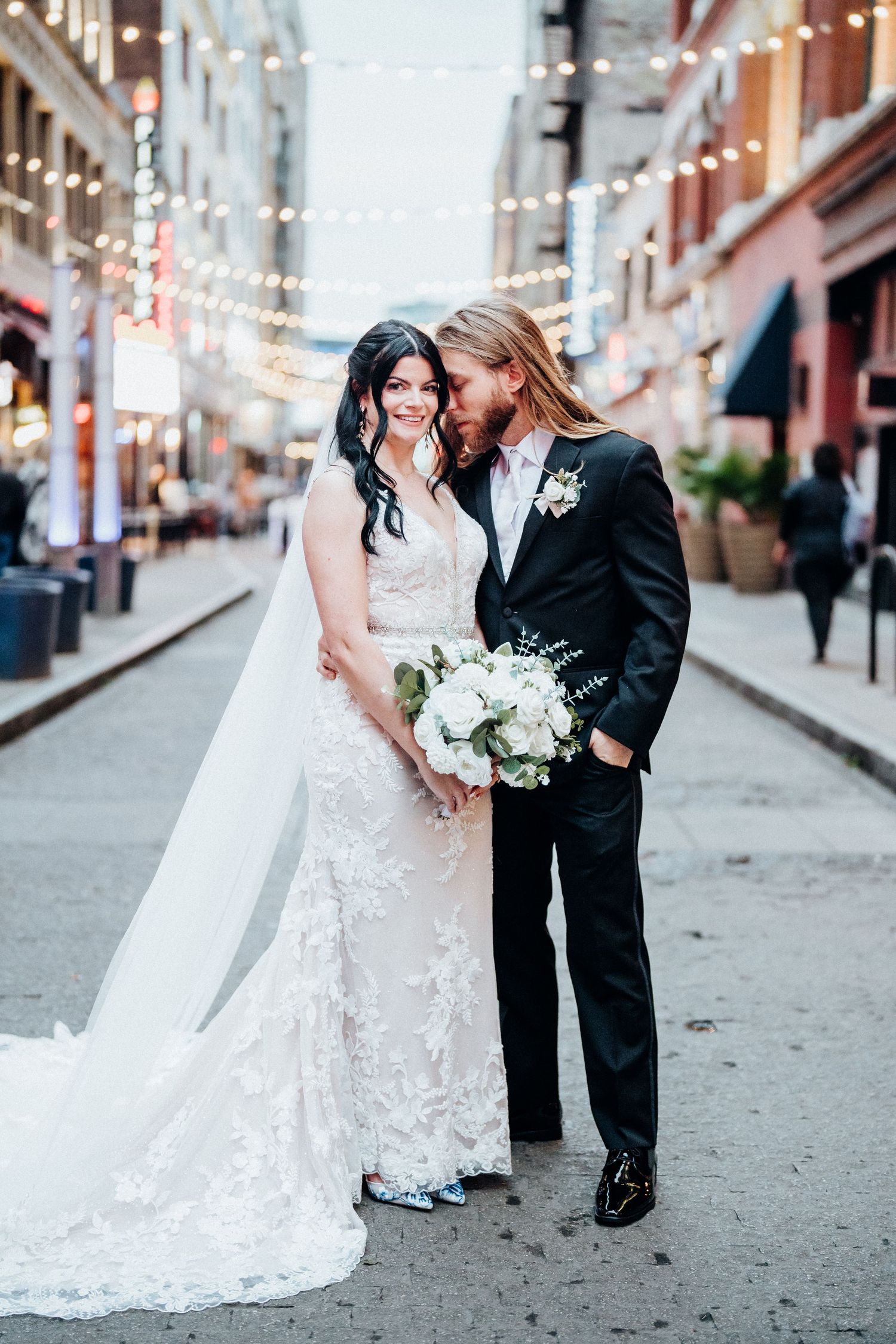 A romantic city street portrait with string lights and elegant white bouquet.
