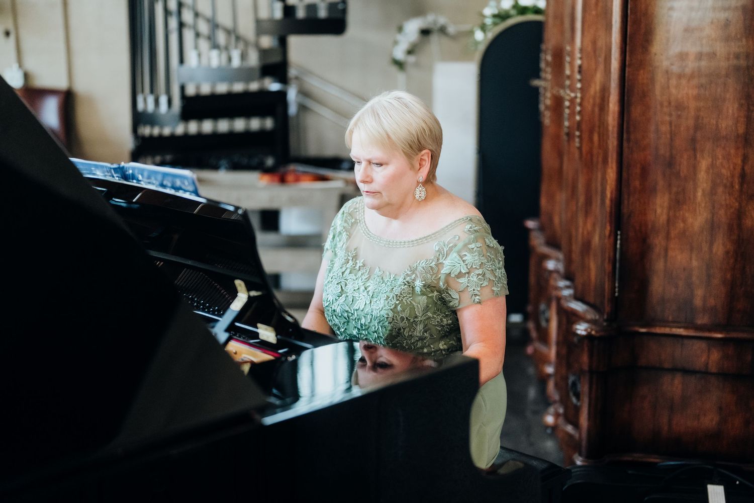 A musician in a sparkly mint green dress performs on a grand piano during an elegant event.
