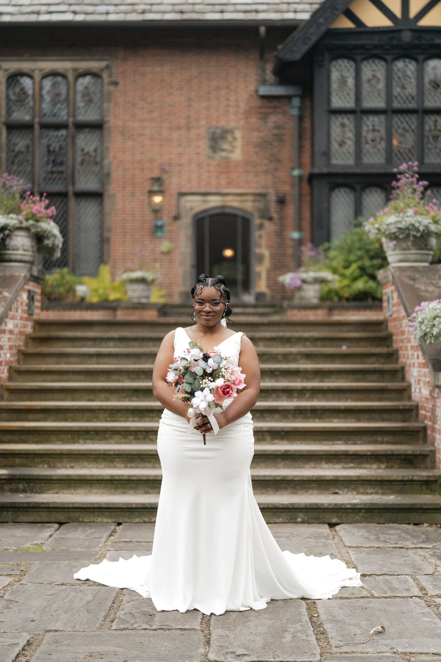 Bride in white dress poses on stone steps in front of historic brick building.