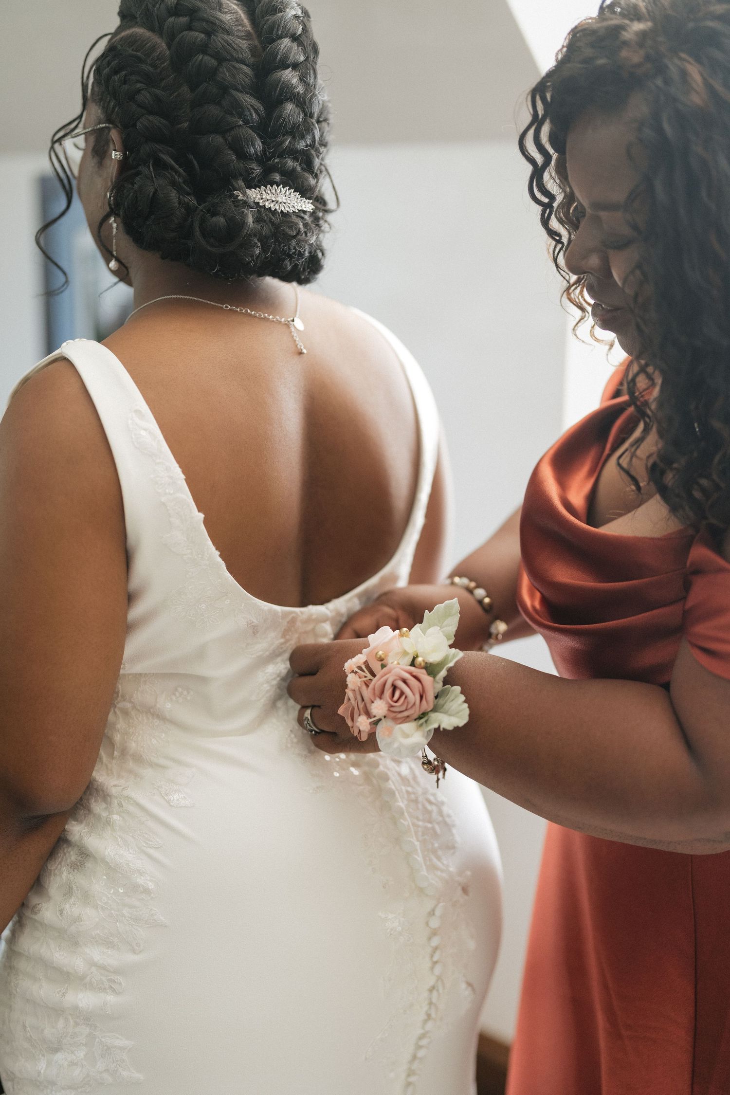 Wedding dress details and bridesmaids in coral dresses helping with final preparations.