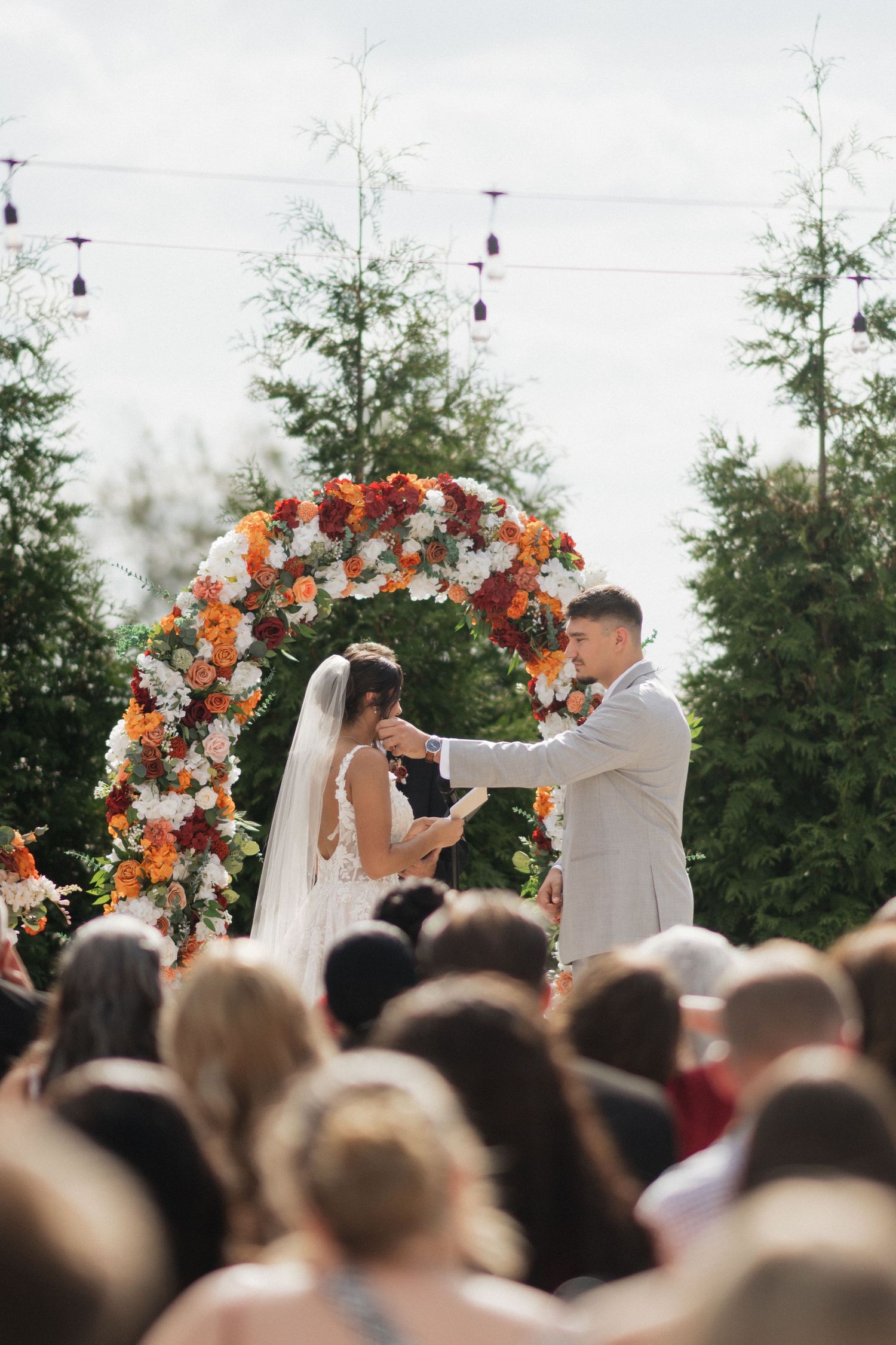 Outdoor wedding ceremony under floral arch with orange and white flowers.