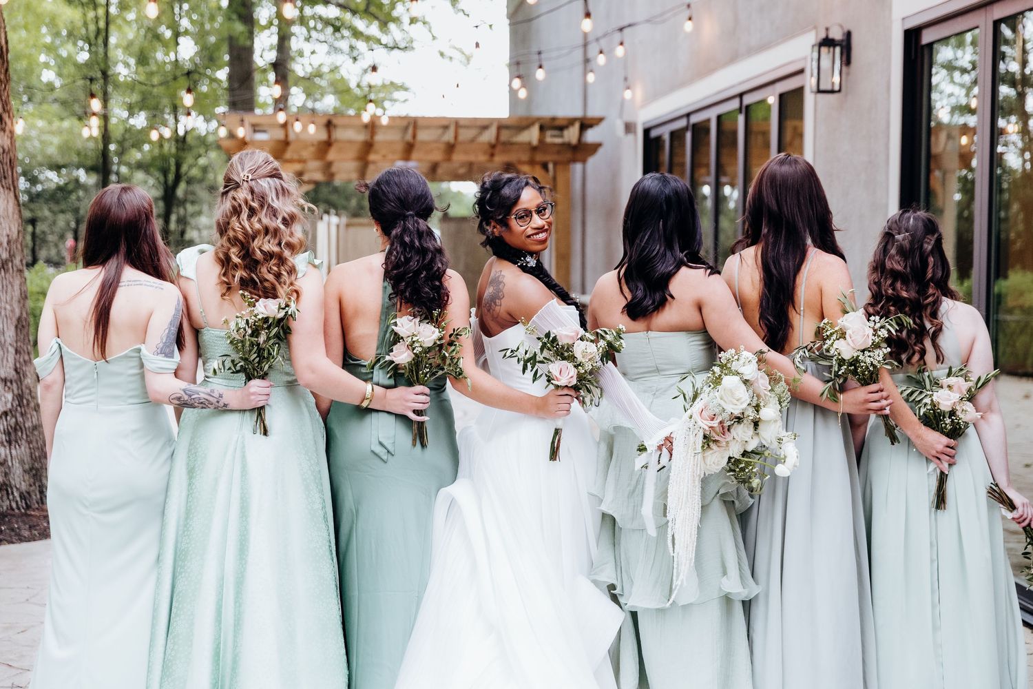 Bridesmaids in mint green dresses standing in a row holding bouquets.