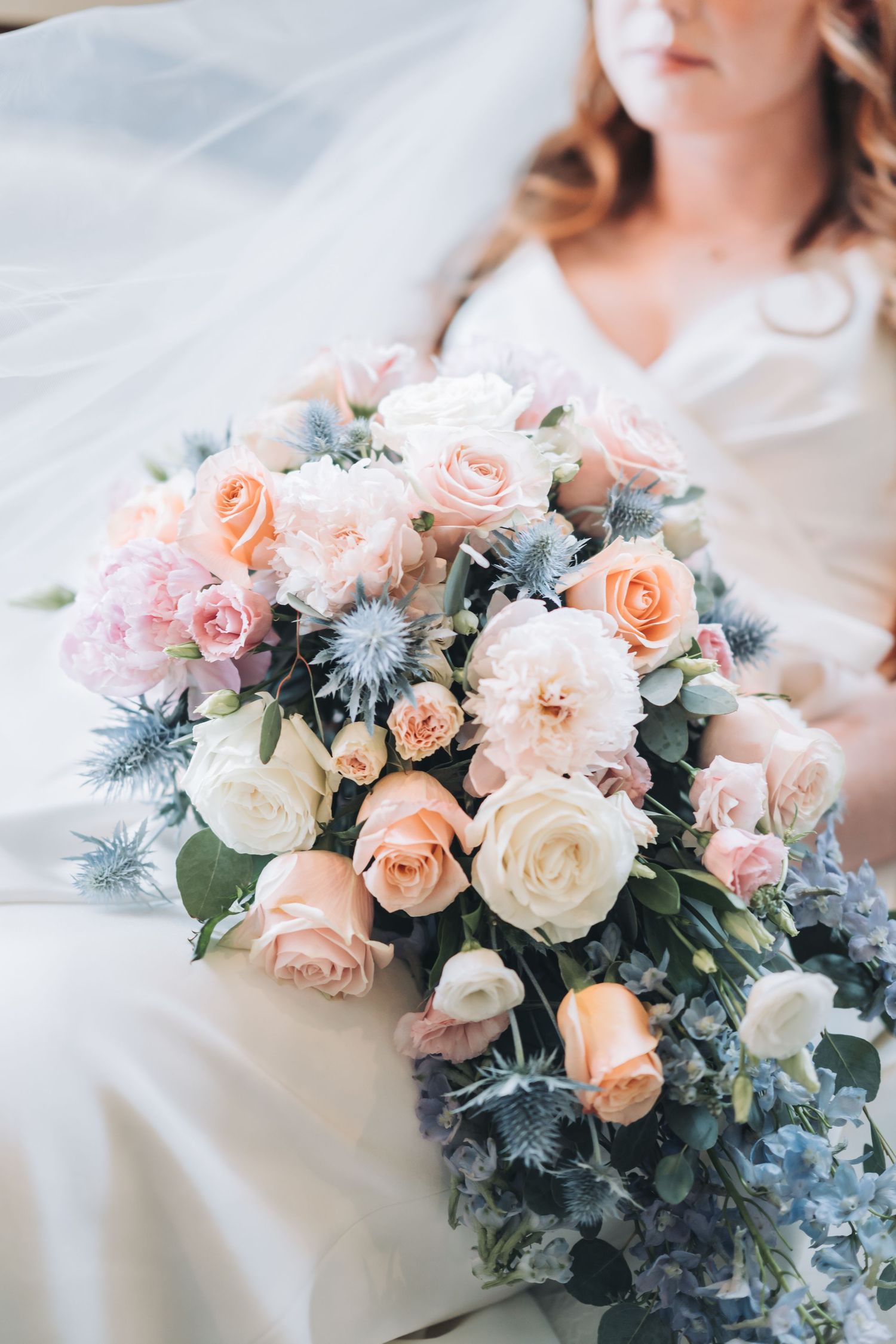 A stunning bridal bouquet featuring blush roses, white roses, and blue accents rests on white fabric.