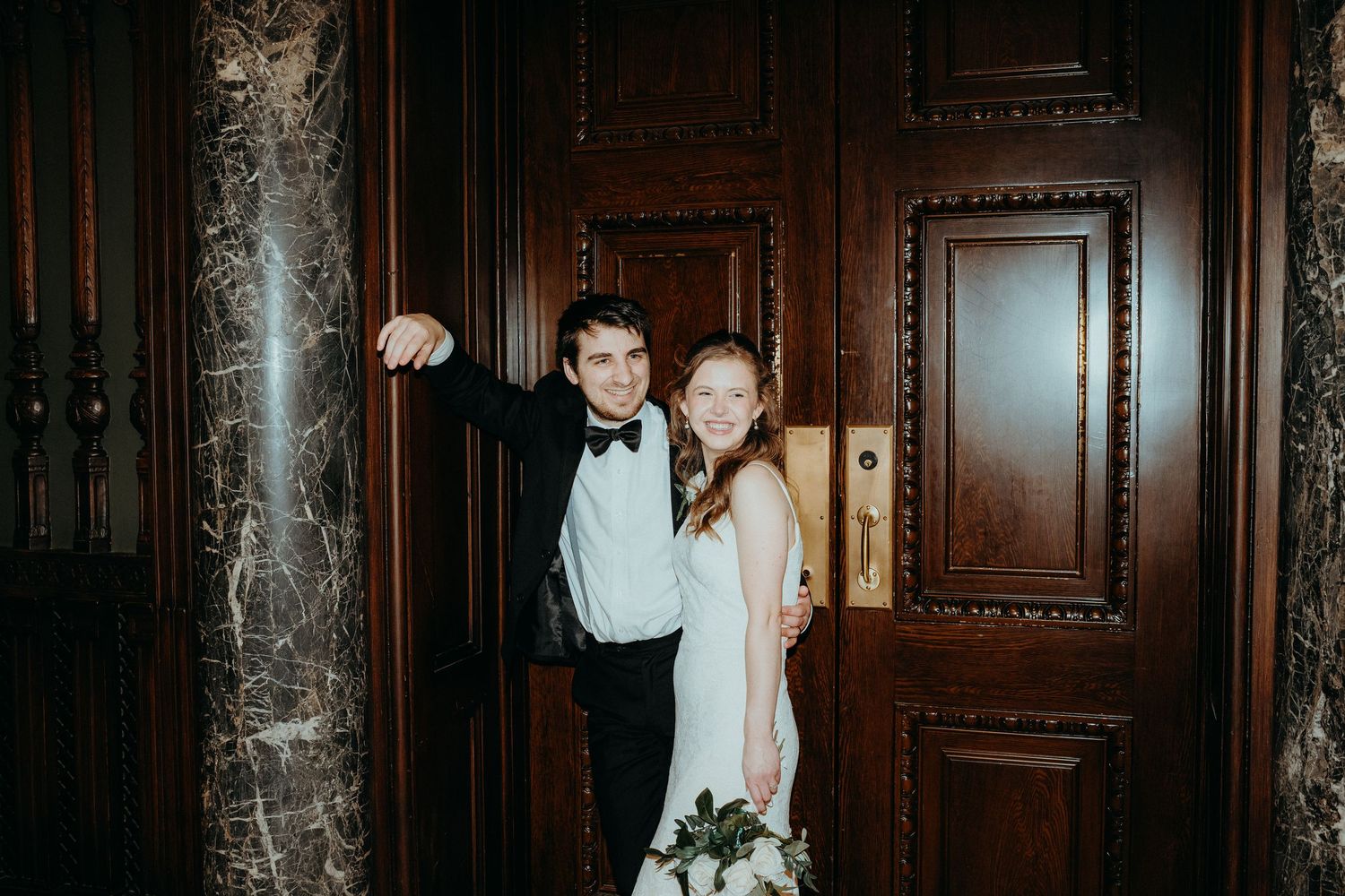 Bride and groom posing together in front of elegant wooden doors at the Cleveland public library for a Cleveland wedding