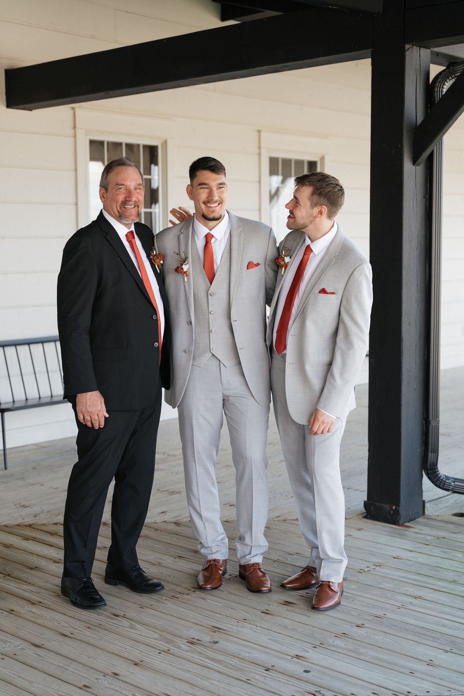 Wedding party members in gray suits and red accents pose together on a rustic porch.