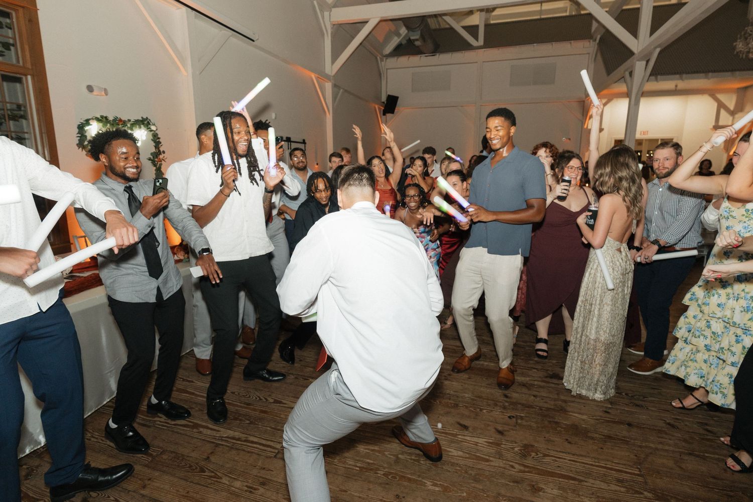 Wedding reception guests dancing and jumping energetically on wooden dance floor.