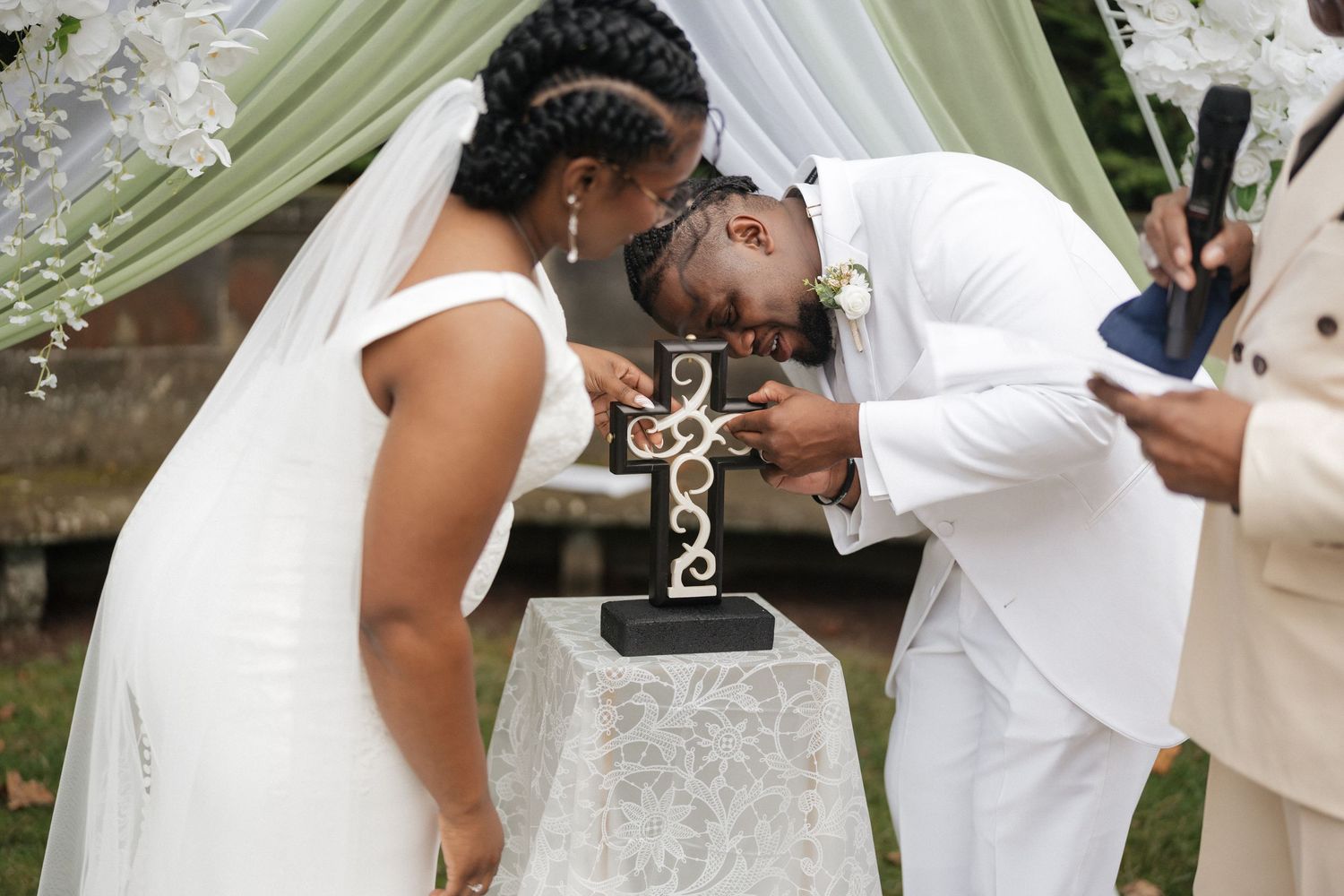 Emotional wedding ceremony exchange under white floral arch.