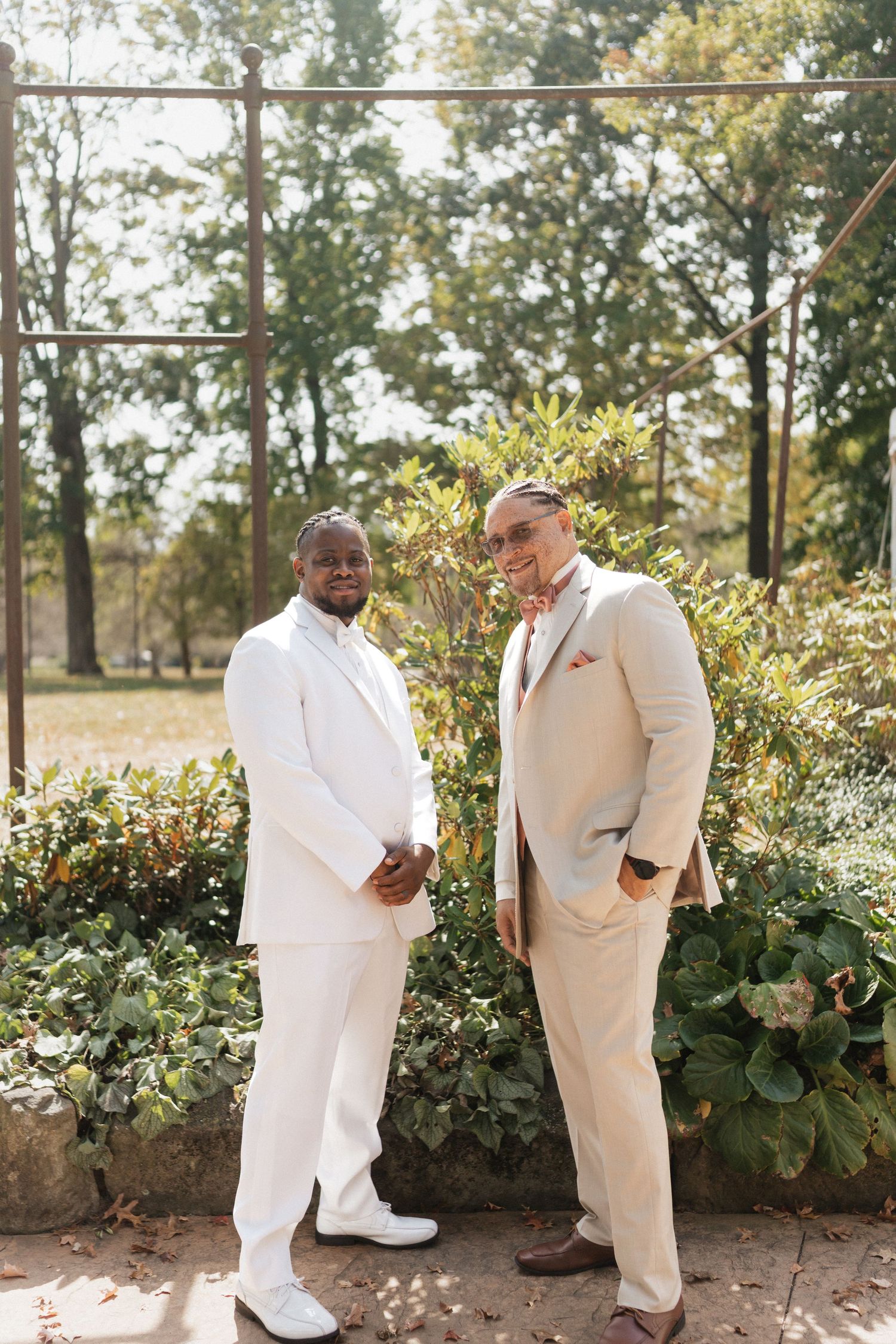 Two people in white formal attire share a candid moment in a garden setting.