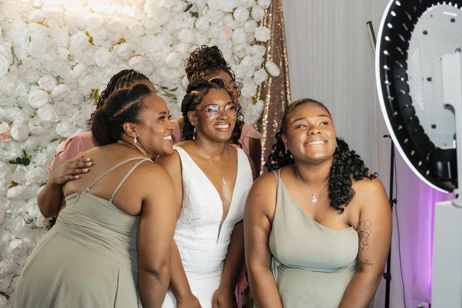 Wedding party members sharing joyful moment in front of white floral wall.