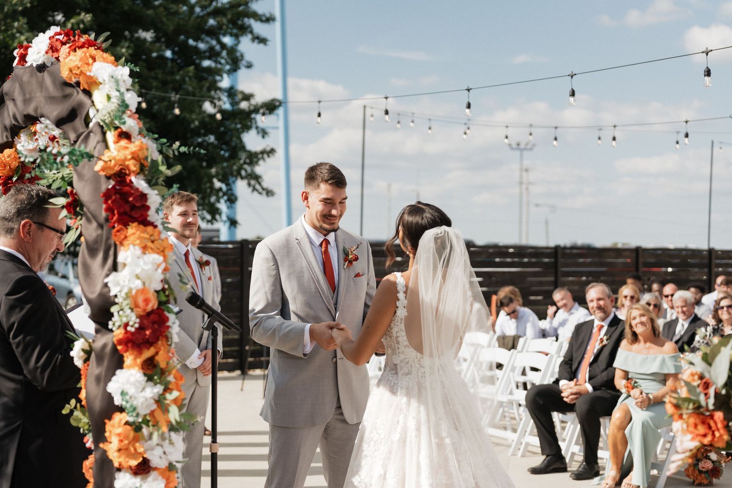Outdoor wedding ceremony with string lights and orange floral decorations.