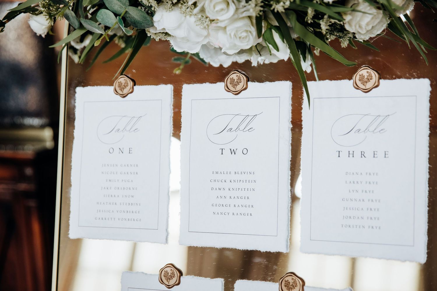 Wedding reception seating cards with floral decorations and wax seals.