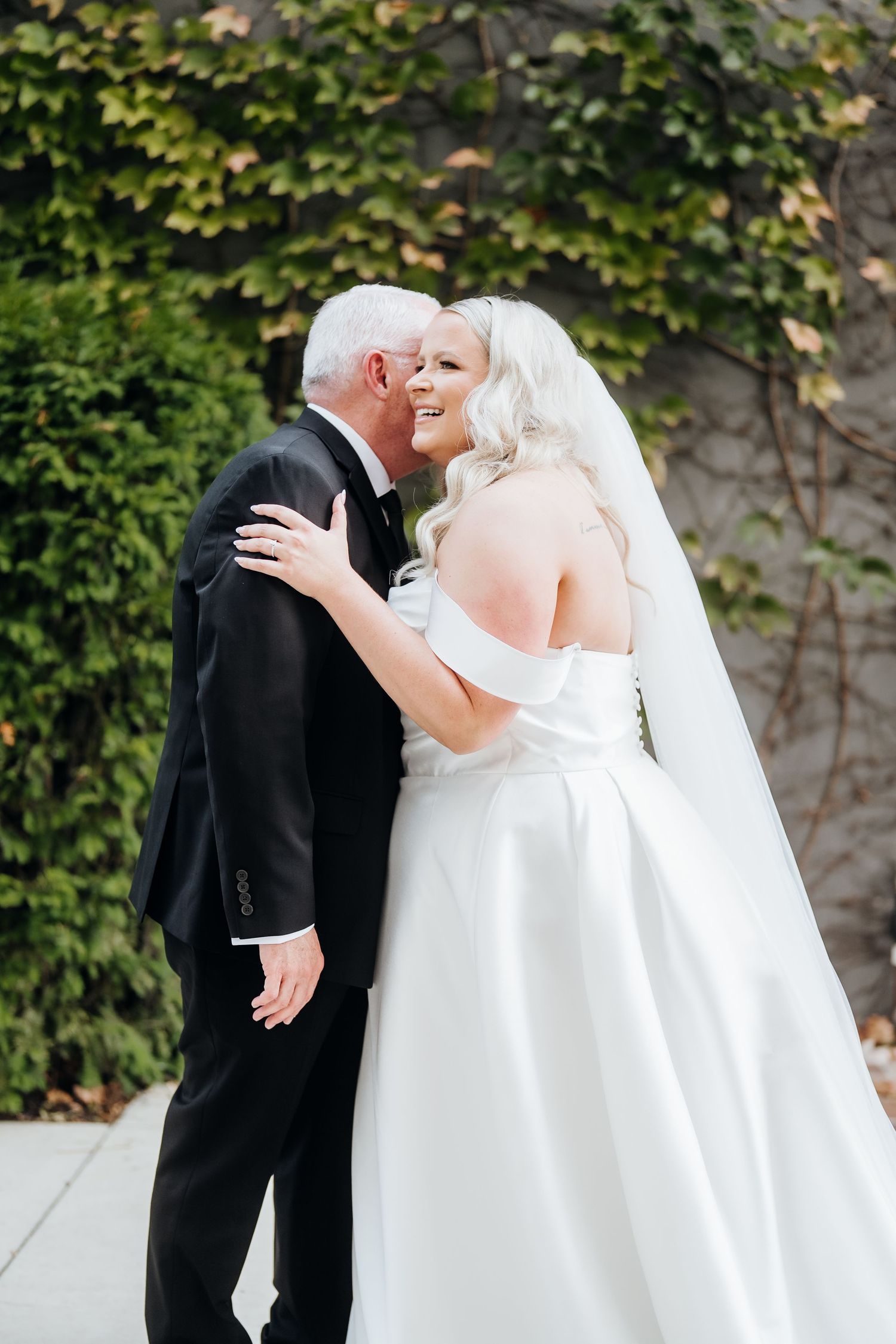 A romantic wedding couple shares an intimate moment against a backdrop of green ivy.