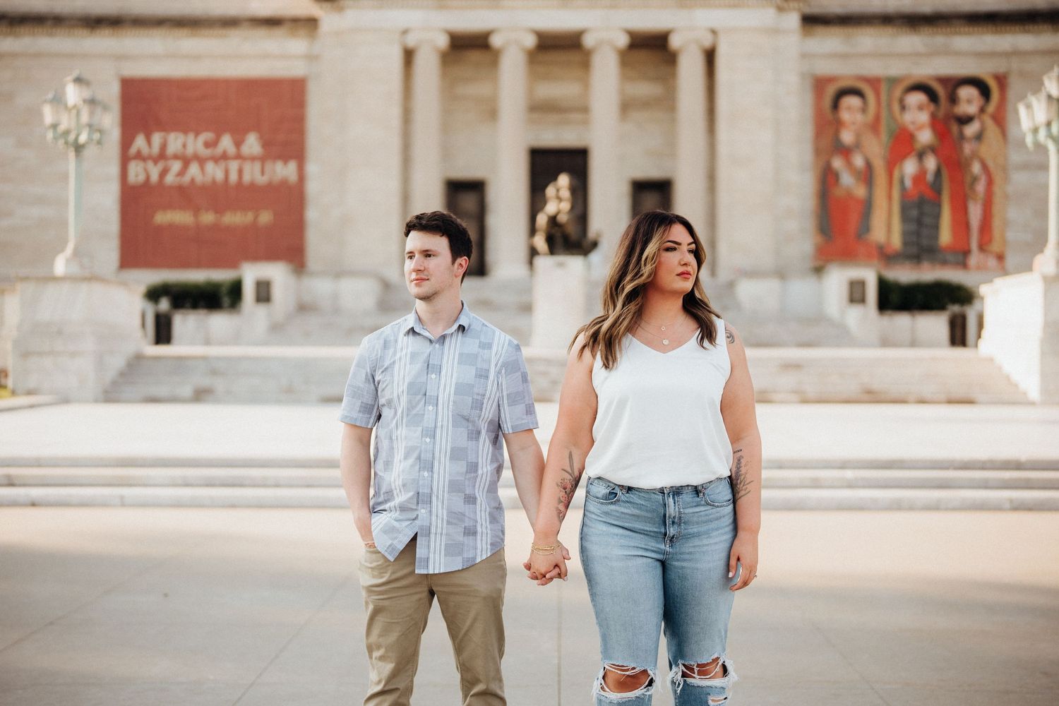 A couple holds hands while standing in front of a museum entrance with banners displayed above.
